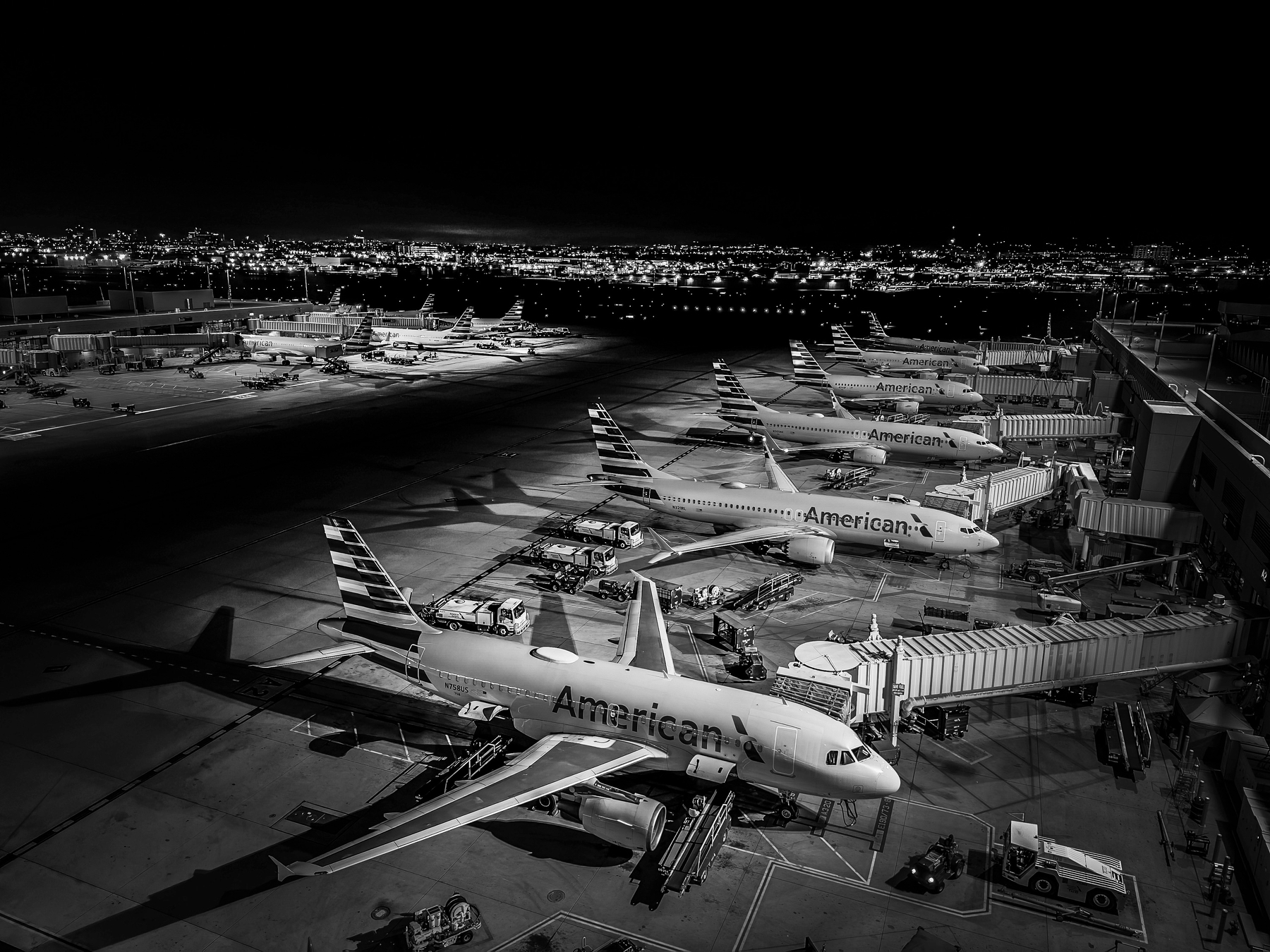 Auto-generated description: Multiple airplanes are parked at an airport terminal at night with a cityscape in the background.