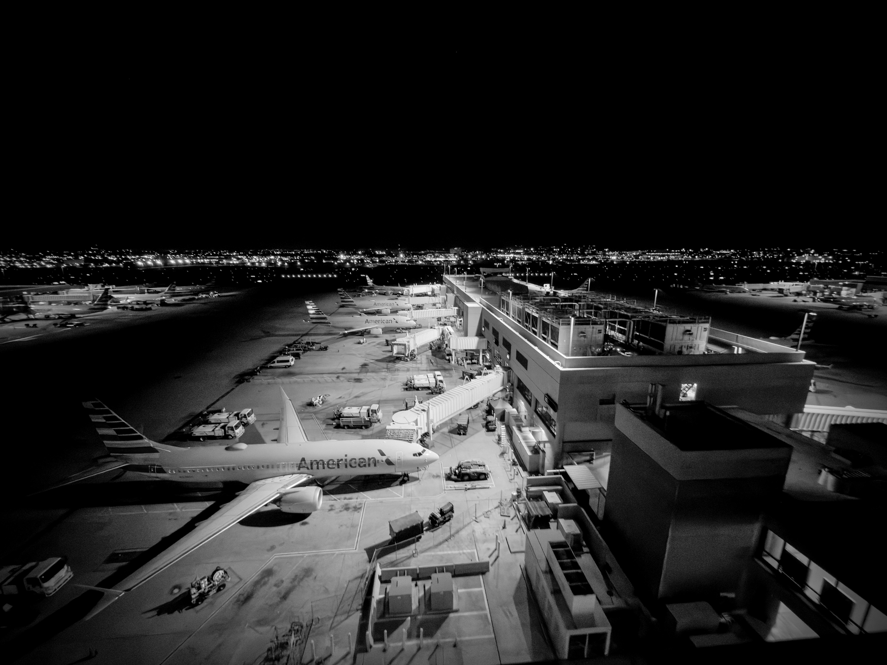 Auto-generated description: An airport terminal at night is bustling with several airplanes parked at gates, illuminated by airport lights.