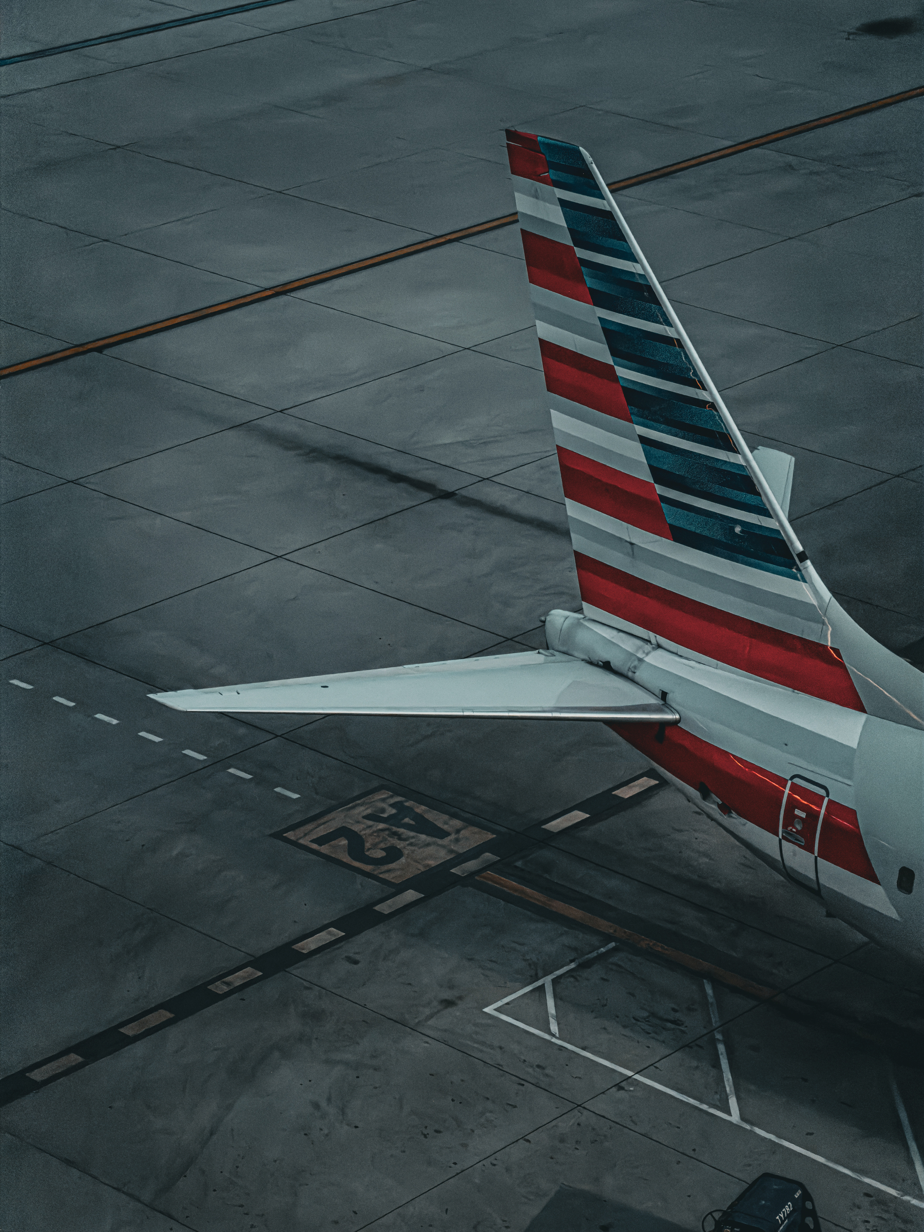 Auto-generated description: The tail section of an airplane with an American Airlines logo is parked on an airport tarmac.