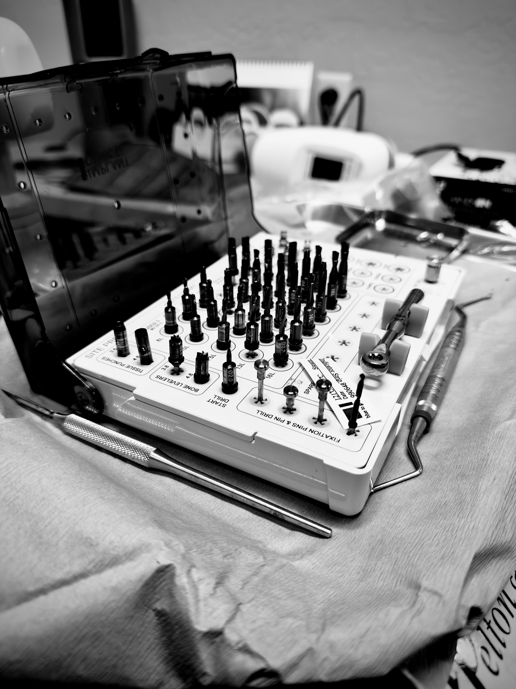 Auto-generated description: A black and white photo displays a dental tool kit with various instruments and bits arranged neatly on a tray in a clinical setting.