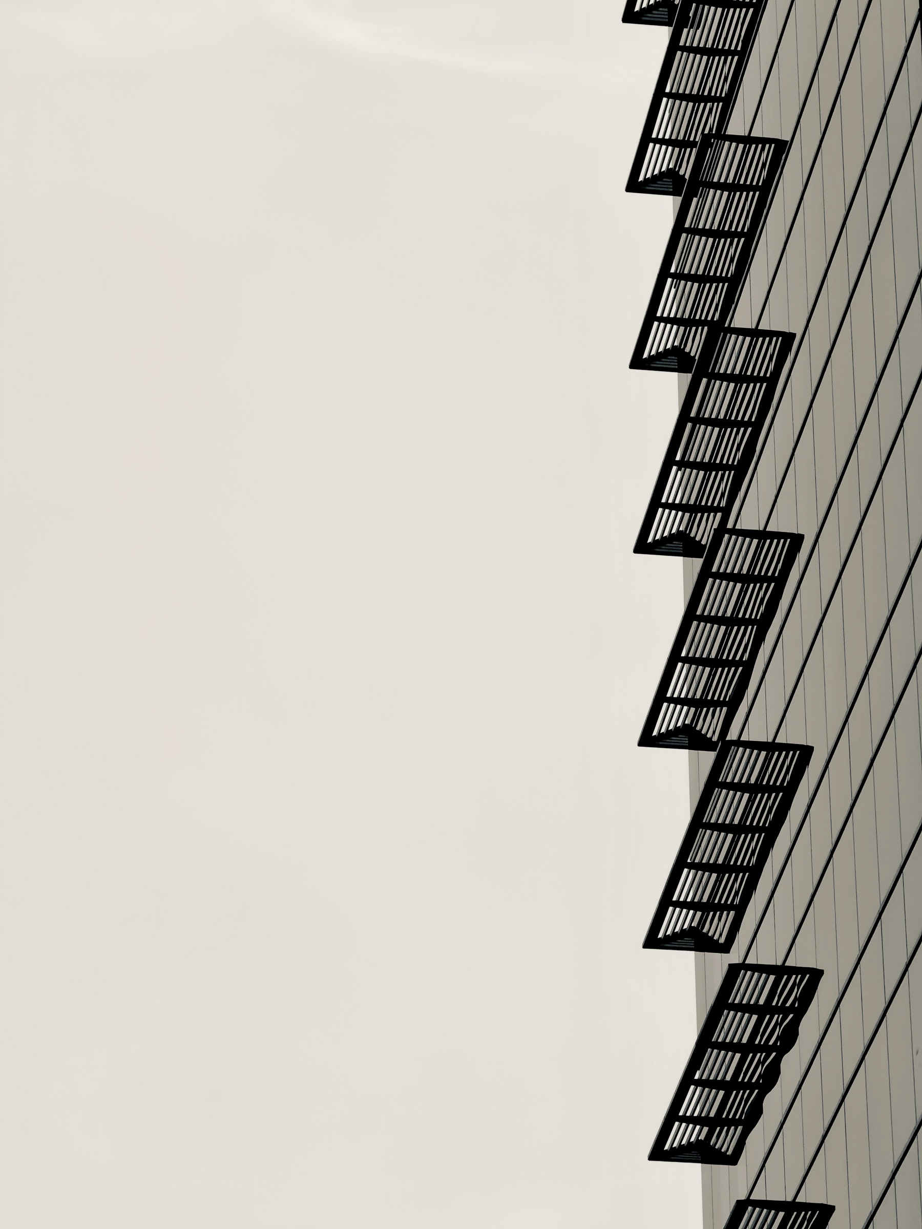 Auto-generated description: A modern building facade features a series of evenly spaced balconies casting strong shadows against a clear, pale sky.