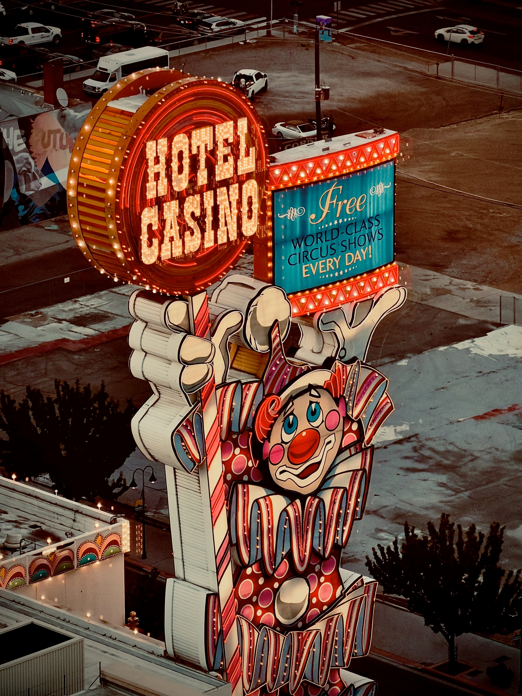 Auto-generated description: A brightly lit vintage-style sign features a clown holding circular HOTEL CASINO lights and advertising free world-class circus shows every day.