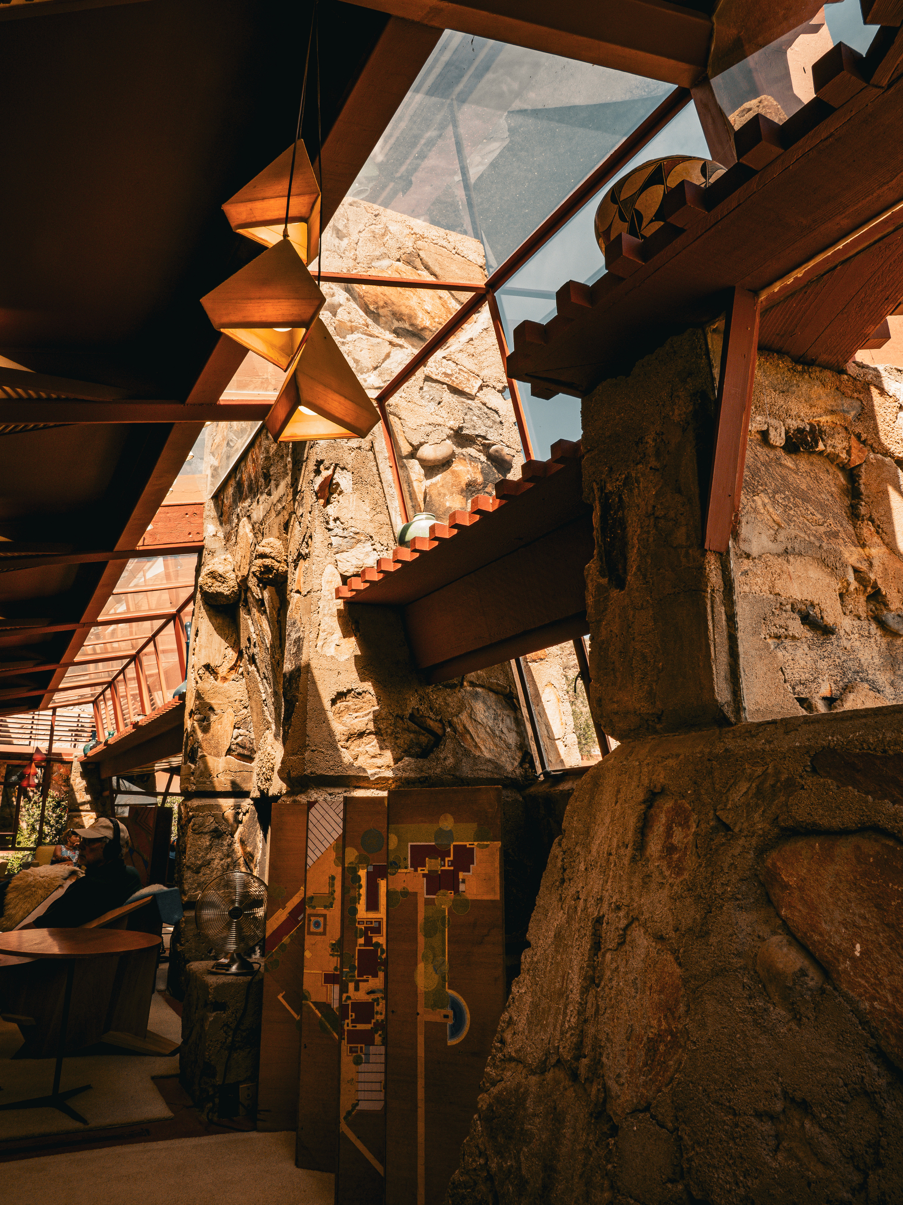 Auto-generated description: A room with stone walls and a slanted glass ceiling features architectural models and angular light fixtures.