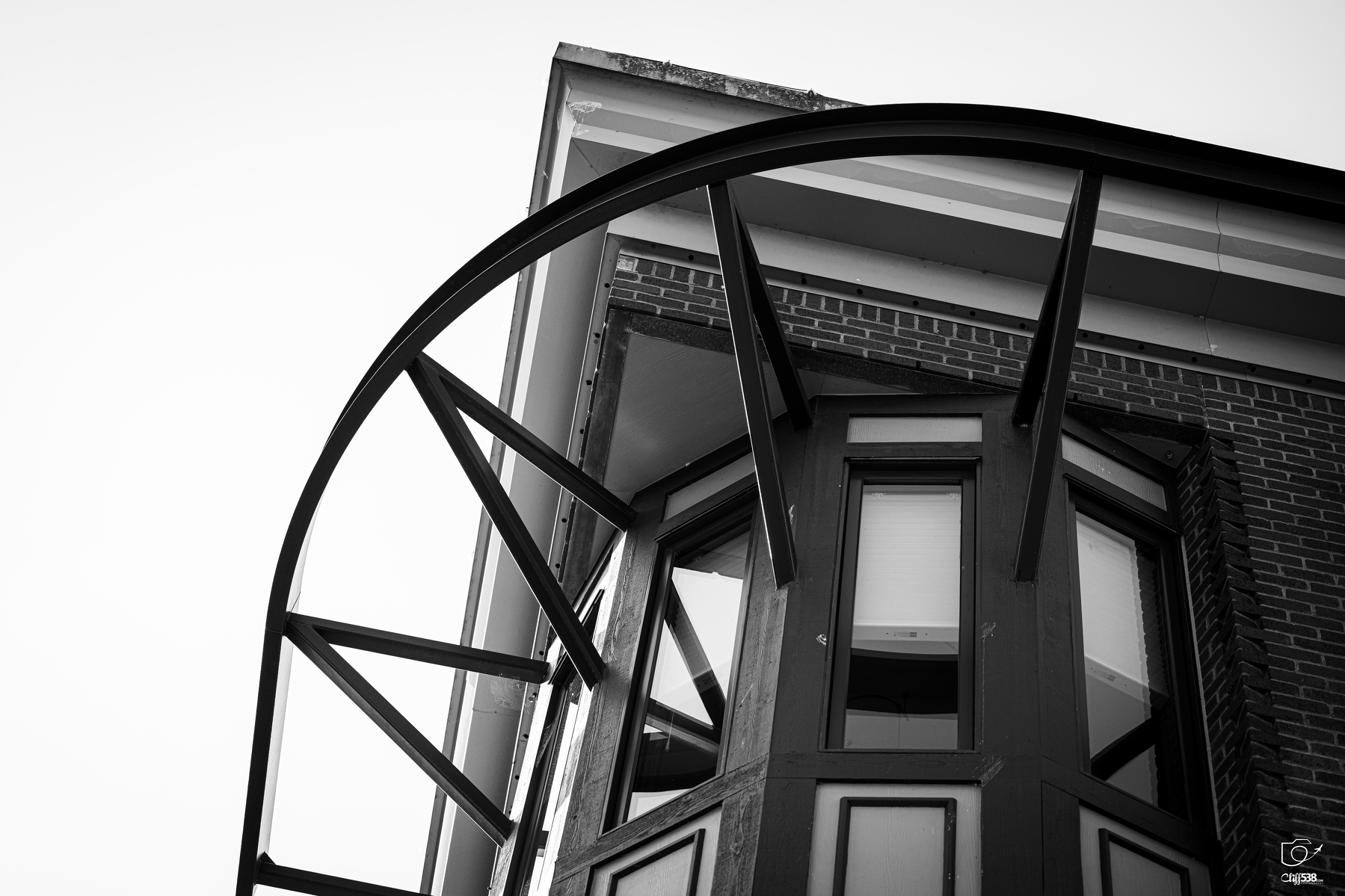 Auto-generated description: A close-up view of a building corner features large windows and a geometric metal structure arching above.