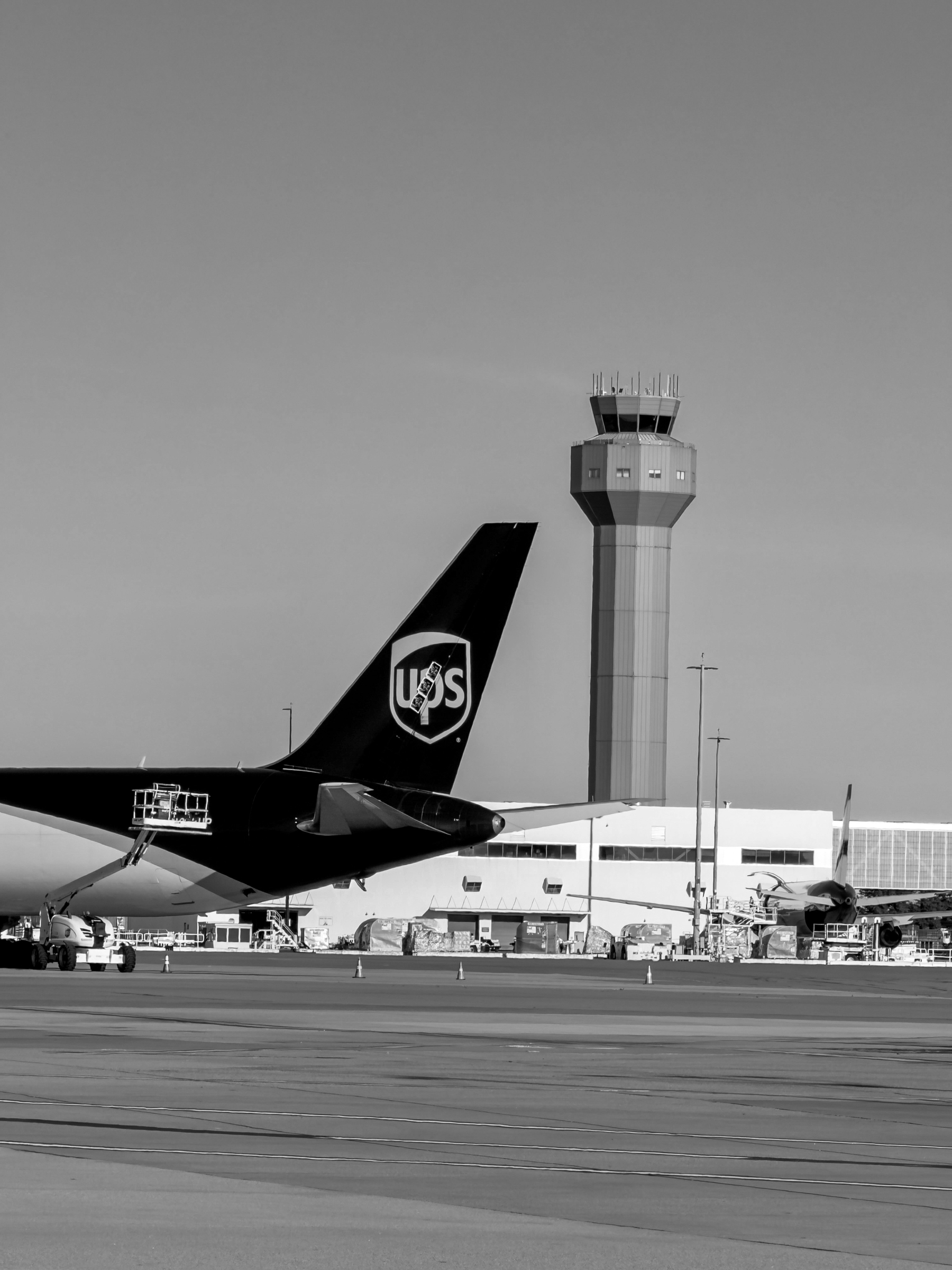 Auto-generated description: An airport scene shows a UPS cargo plane parked on the tarmac with a control tower visible in the background.