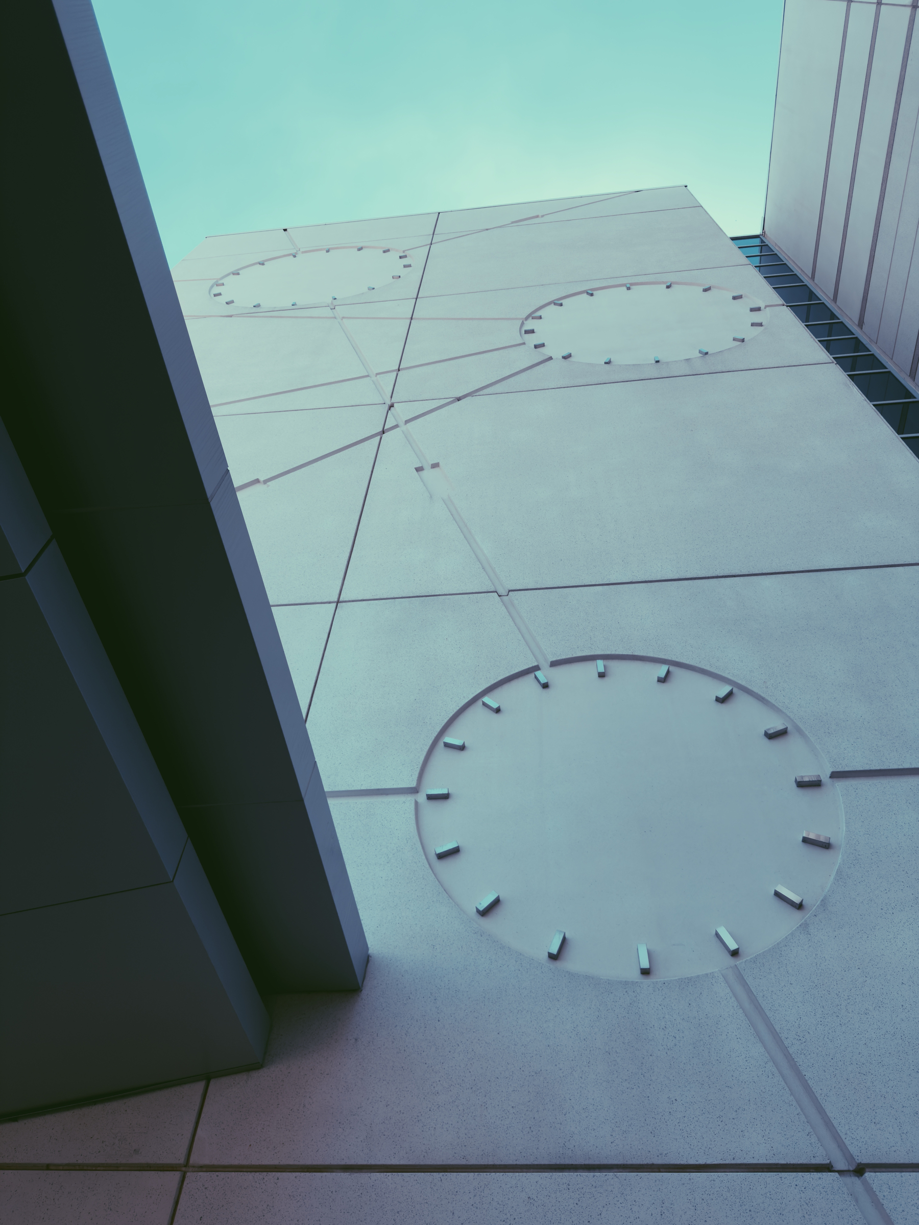 A modern building facade features large circular patterns and geometric lines against a blue sky.