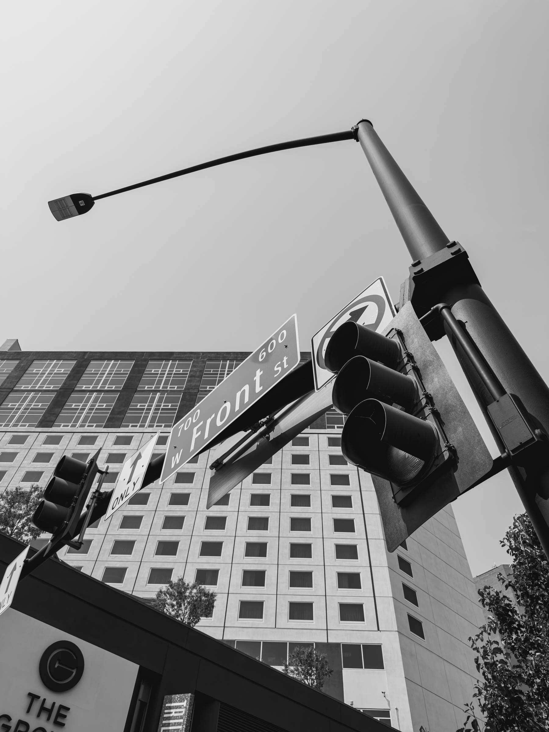 Auto-generated description: A traffic light, street signs including one for W Front St, and a tall building are captured from a low angle in black and white.