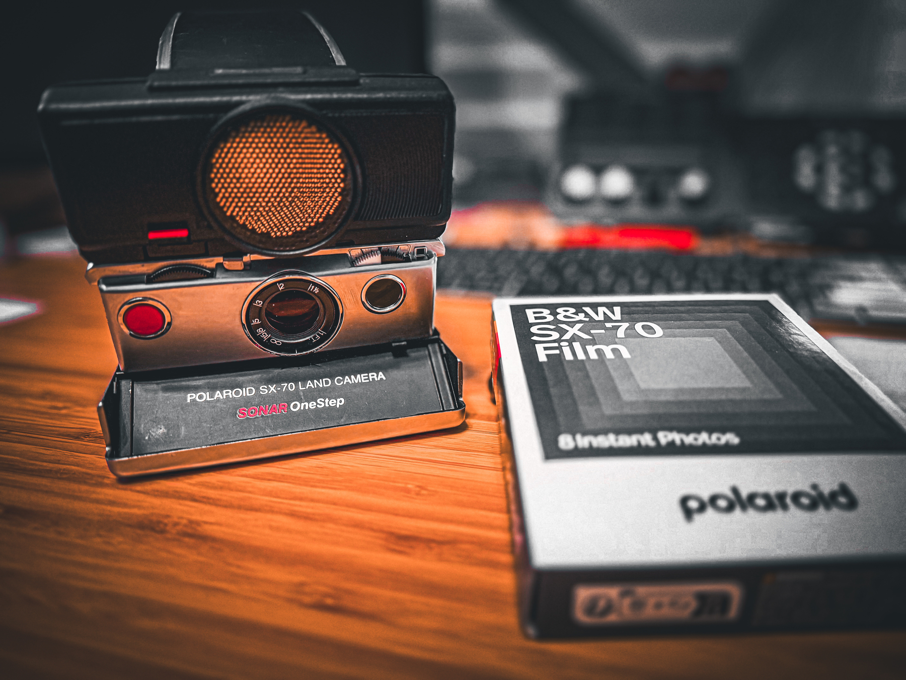 Auto-generated description: A vintage Polaroid SX-70 Land Camera and a box of B&W SX-70 film are placed on a wooden surface.