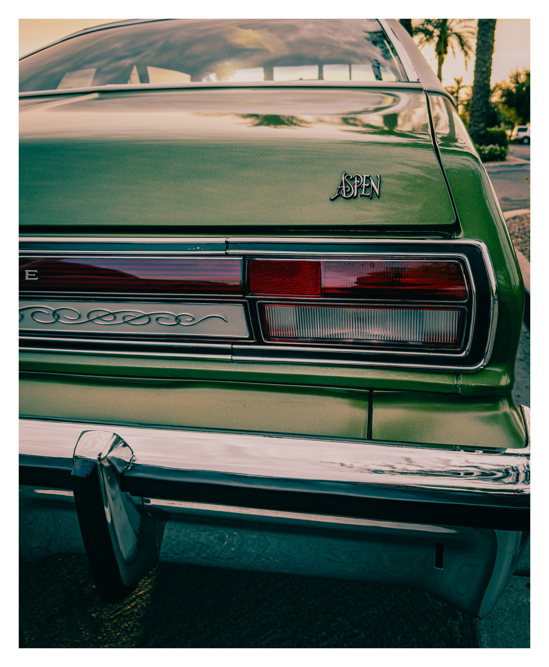 Auto-generated description: A vintage green Aspen car is shown from the rear with its tail light and chrome bumper visible.