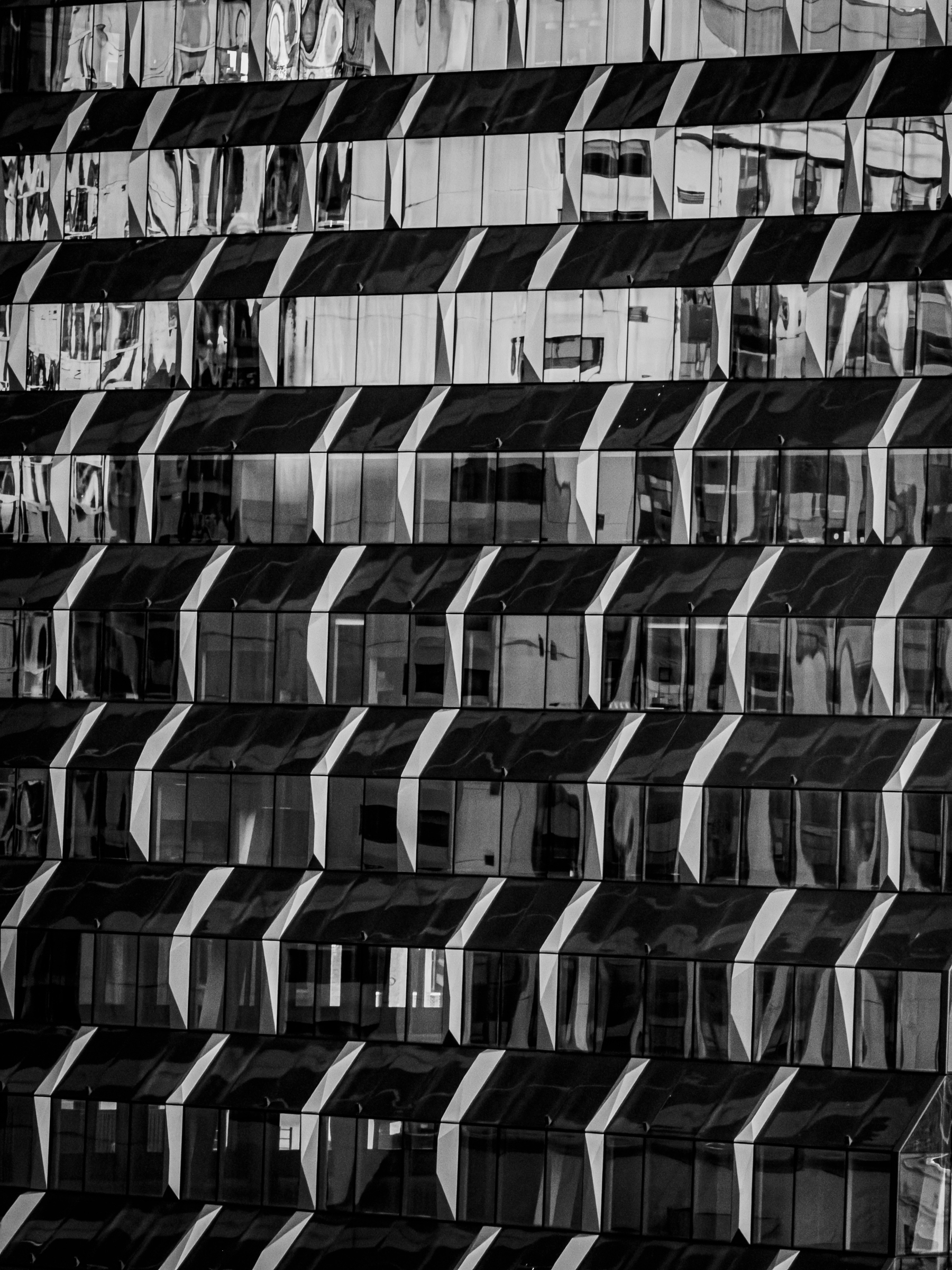 Auto-generated description: A modern building facade features rows of glass windows with reflective surfaces creating abstract patterns and light contrasts.