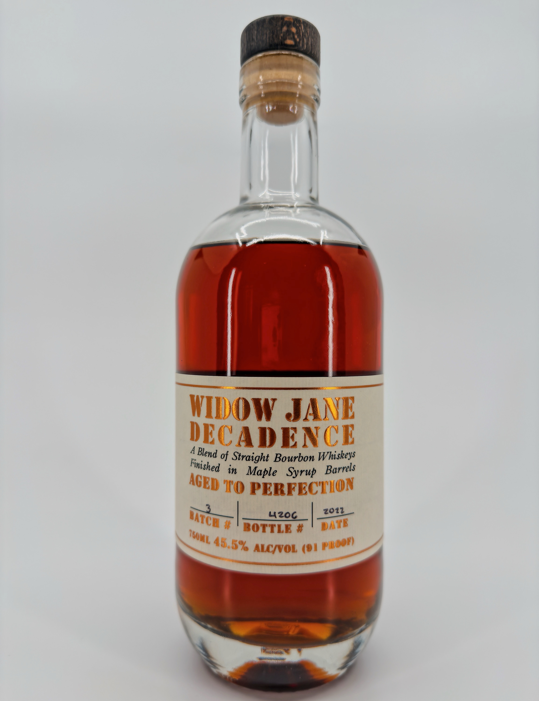 Auto-generated description: A bottle of Widow Jane Decadence bourbon whiskey, aged in maple syrup barrels, is shown with a label detailing its alcohol content and batch information.
