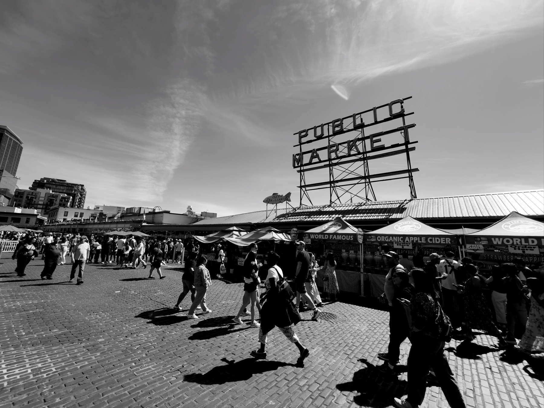 Auto-generated description: People are walking in an outdoor market area with a large sign for Public Market visible against a clear sky.