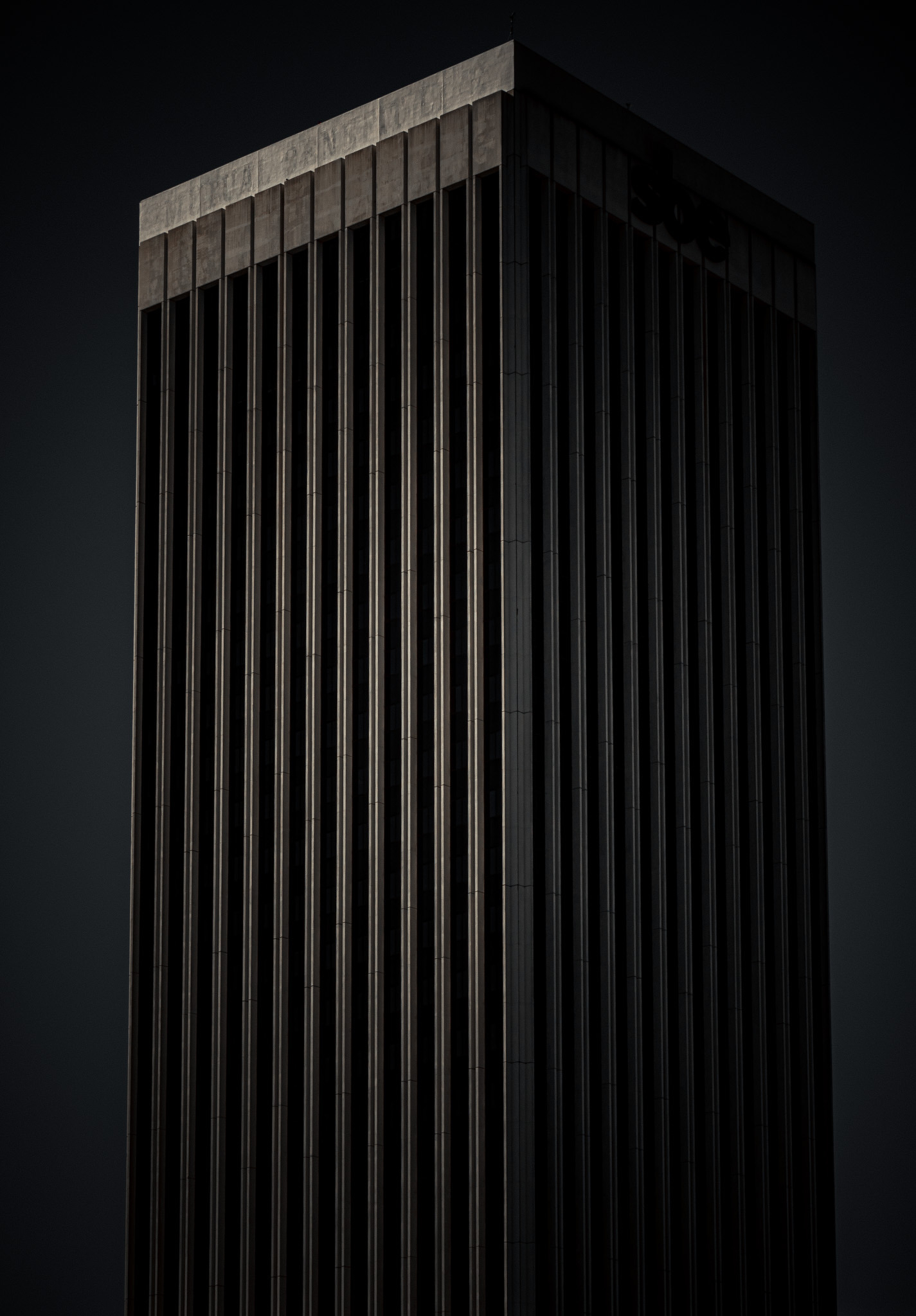 A tall, dark, rectangular skyscraper with vertical lines and minimal lighting.