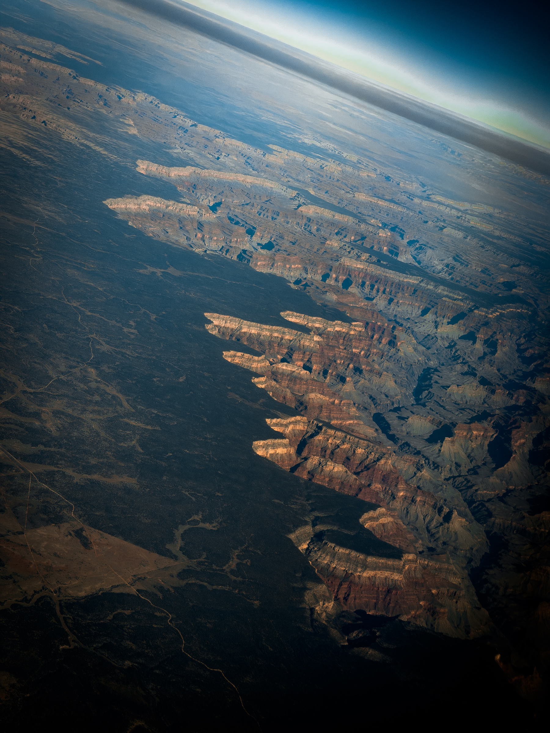 Auto-generated description: A vast canyon landscape with layered rock formations is seen from a high aerial perspective under a clear sky.