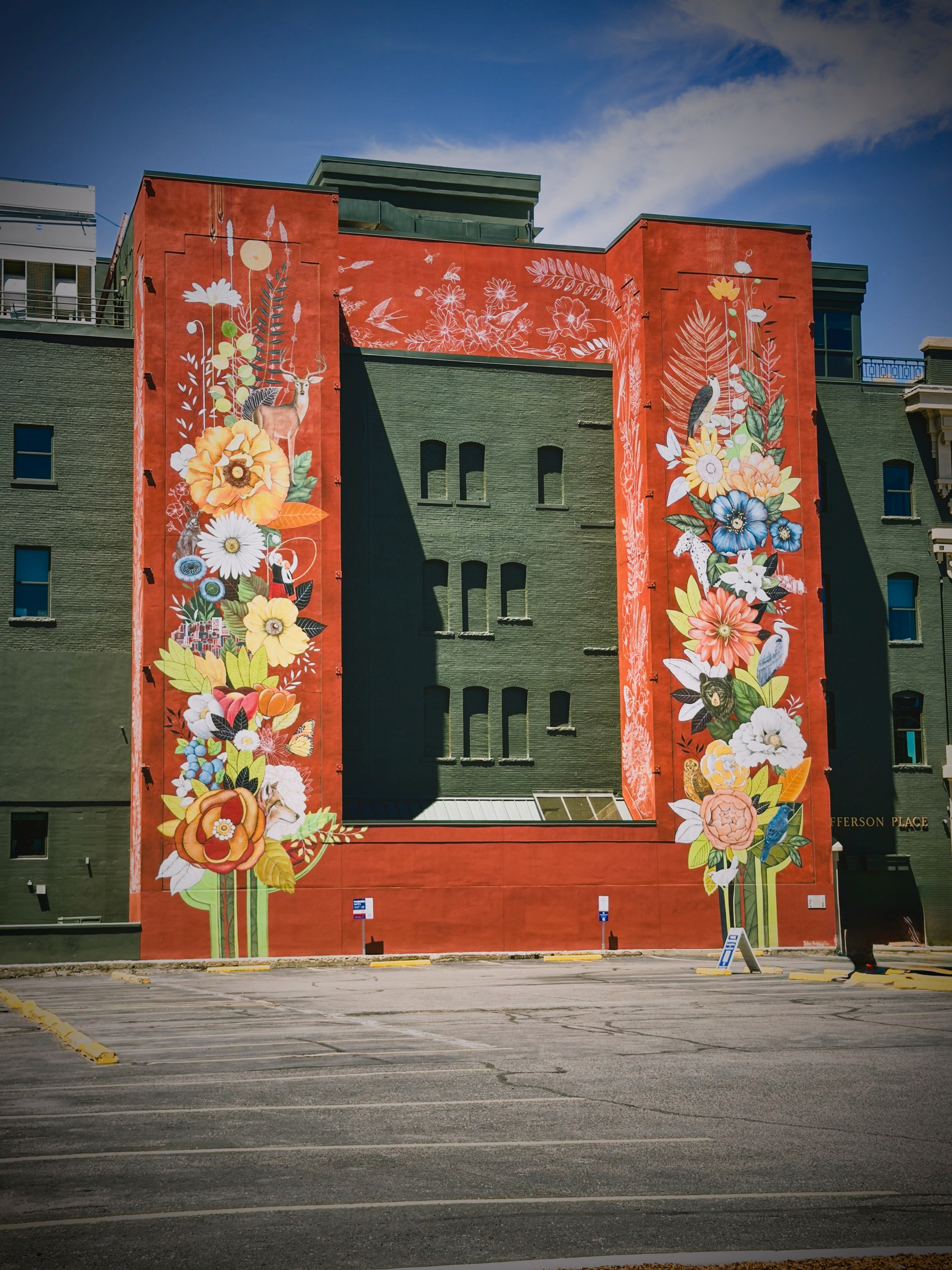 Auto-generated description: A large mural painted on a building features vibrant, oversized flowers and foliage framing a central empty rectangular space.