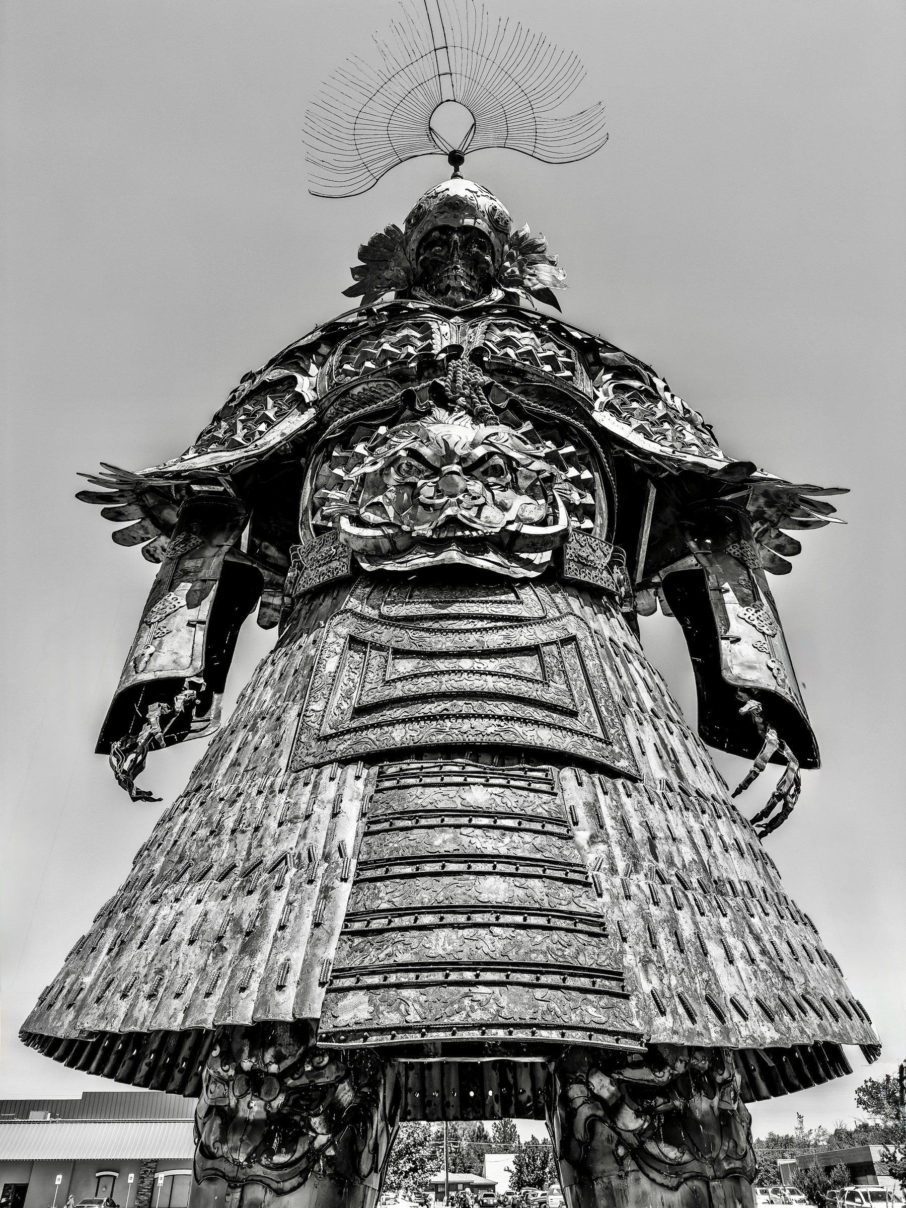 Auto-generated description: A towering statue of a warrior adorned in detailed, ornate armor is viewed from a low angle against a clear sky.