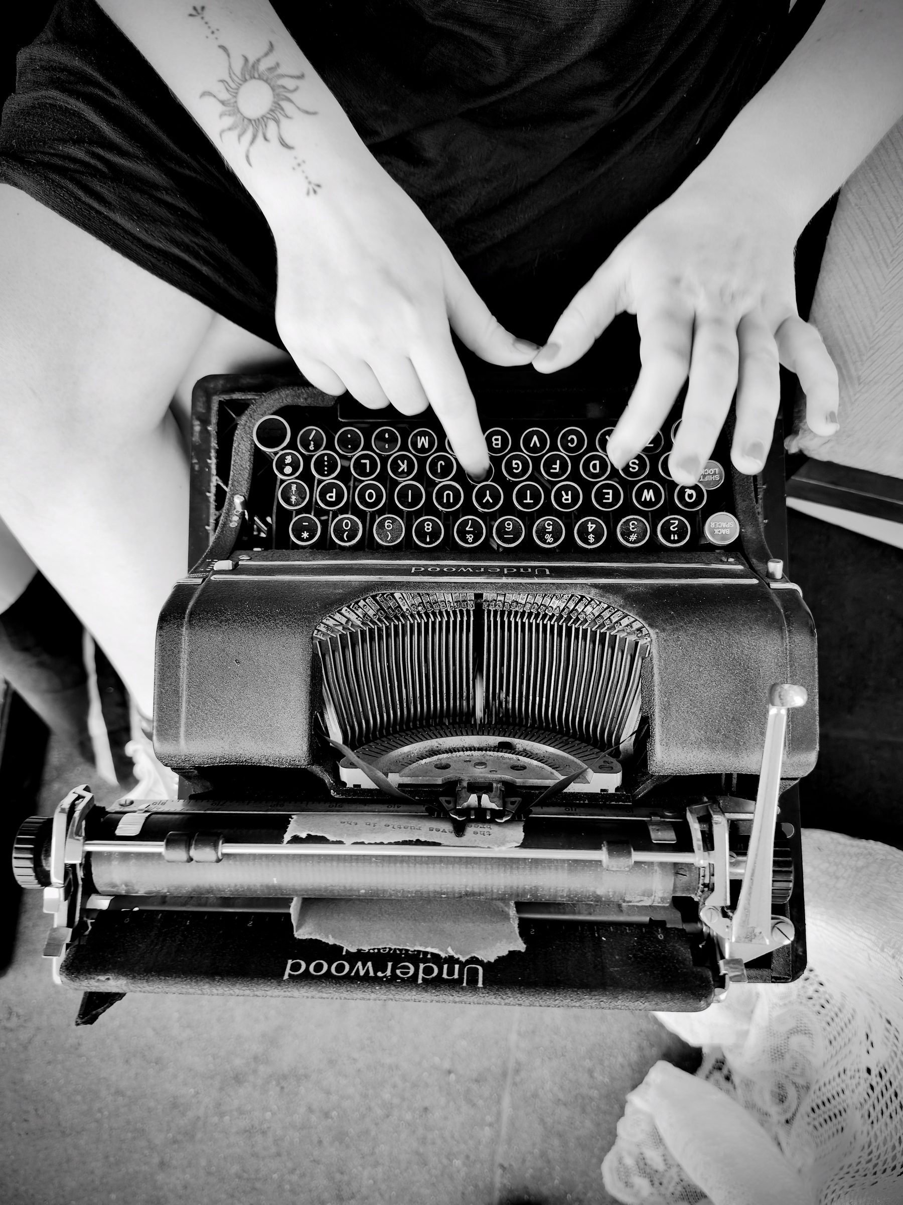 Auto-generated description: A person with a sun tattoo on their forearm is typing on an Underwood typewriter.