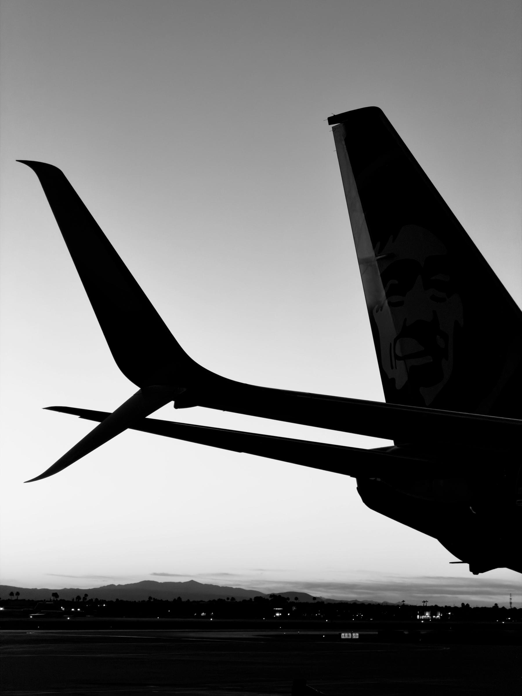 Auto-generated description: An airplane with a distinctive face graphic on its tail is parked on a runway at sunset.