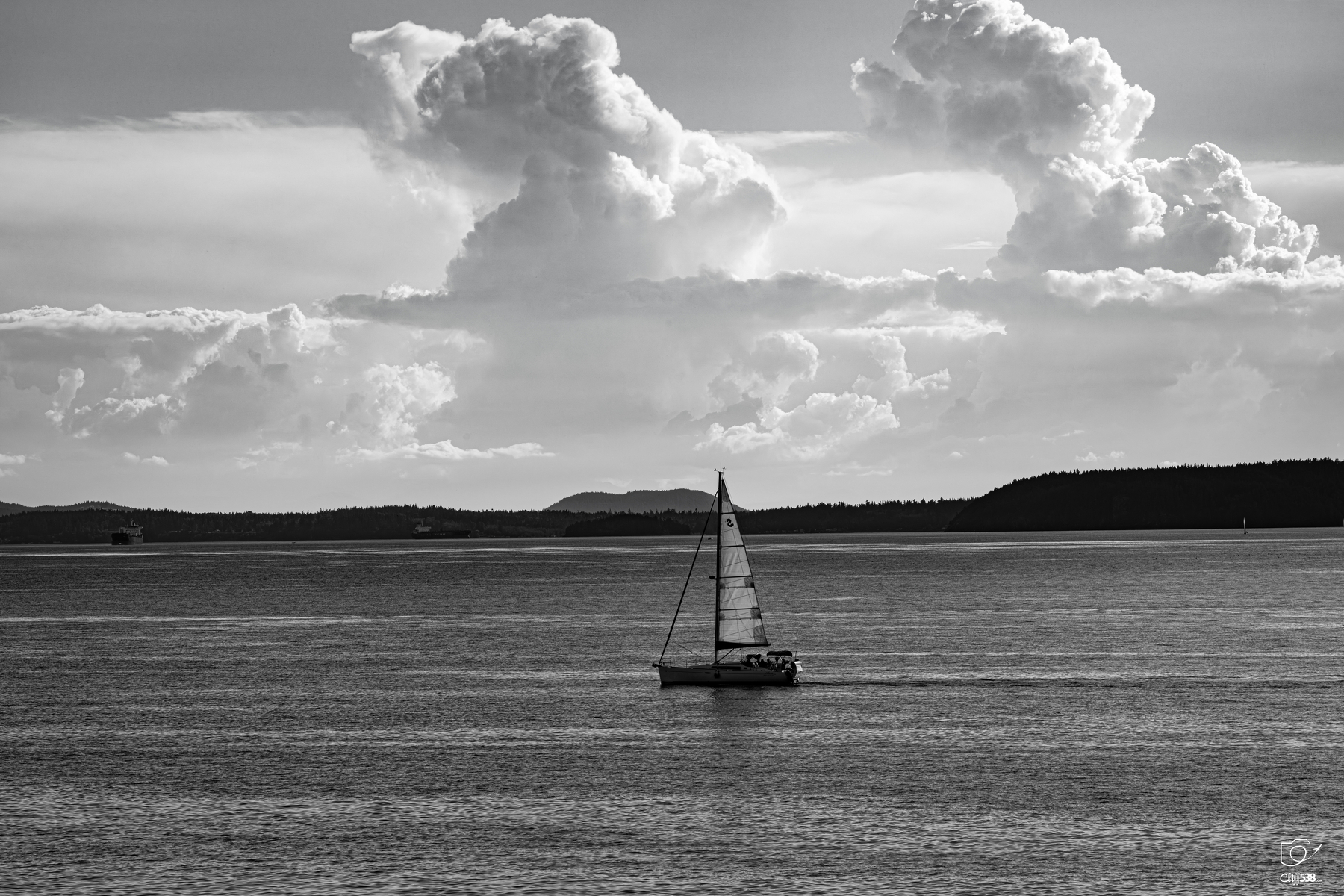Auto-generated description: A lone sailboat glides across calm waters under a sky filled with large, dramatic clouds.