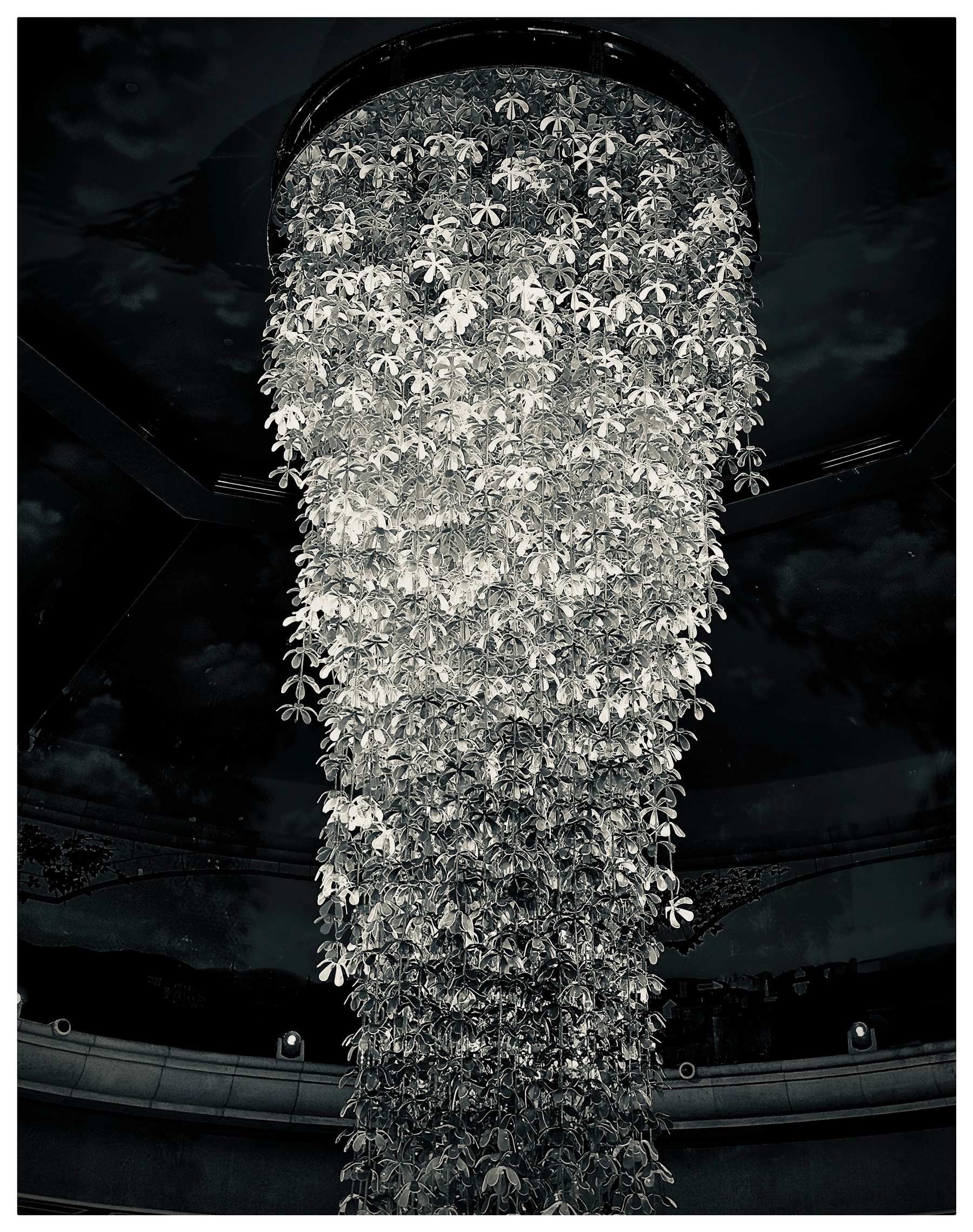 Auto-generated description: A large, intricate chandelier made of numerous small floral elements cascades from the ceiling in a dramatic, elegant display.