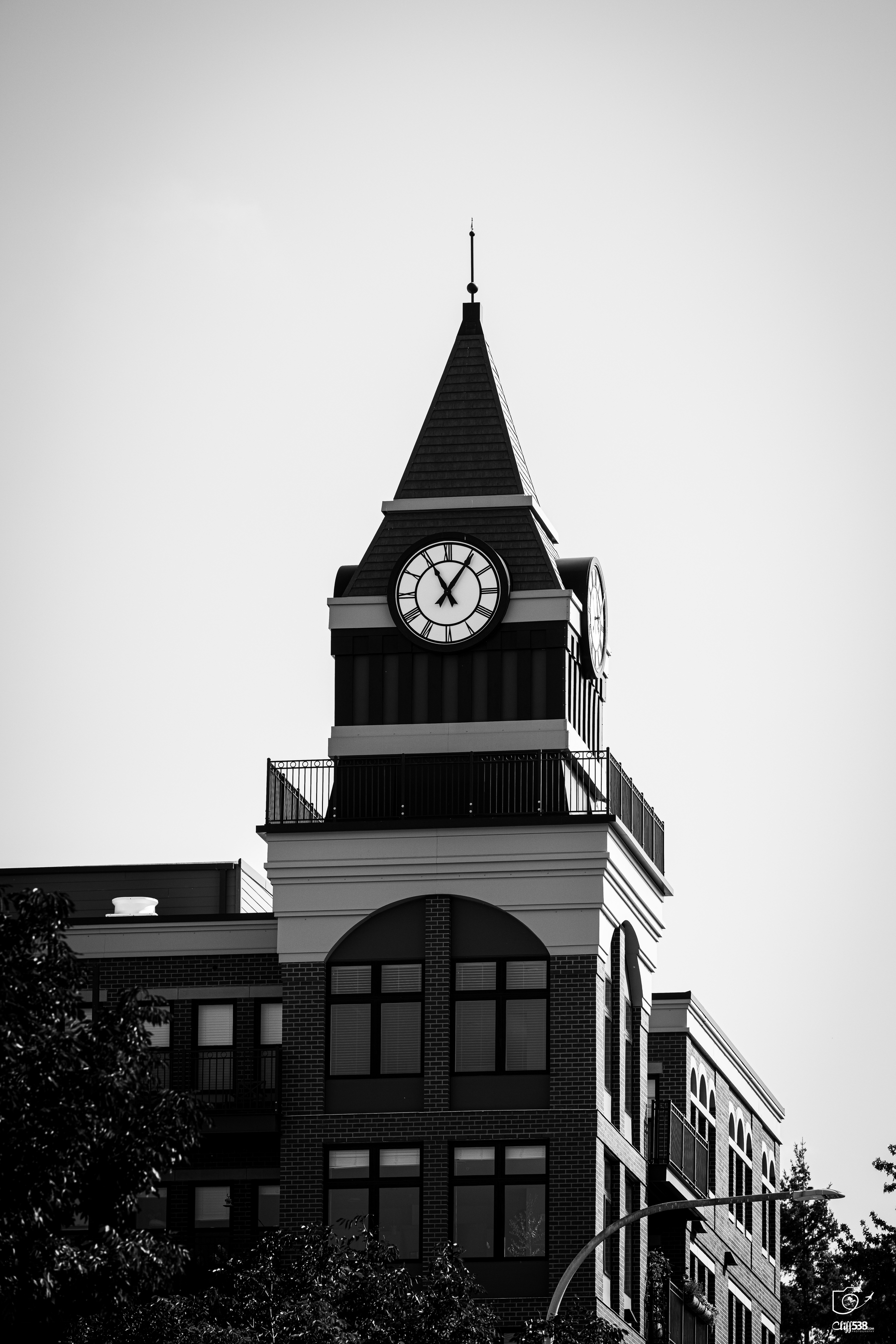 Auto-generated description: A tall clock tower with a pointed roof stands atop a multi-story brick building, showing the time as 11:00.