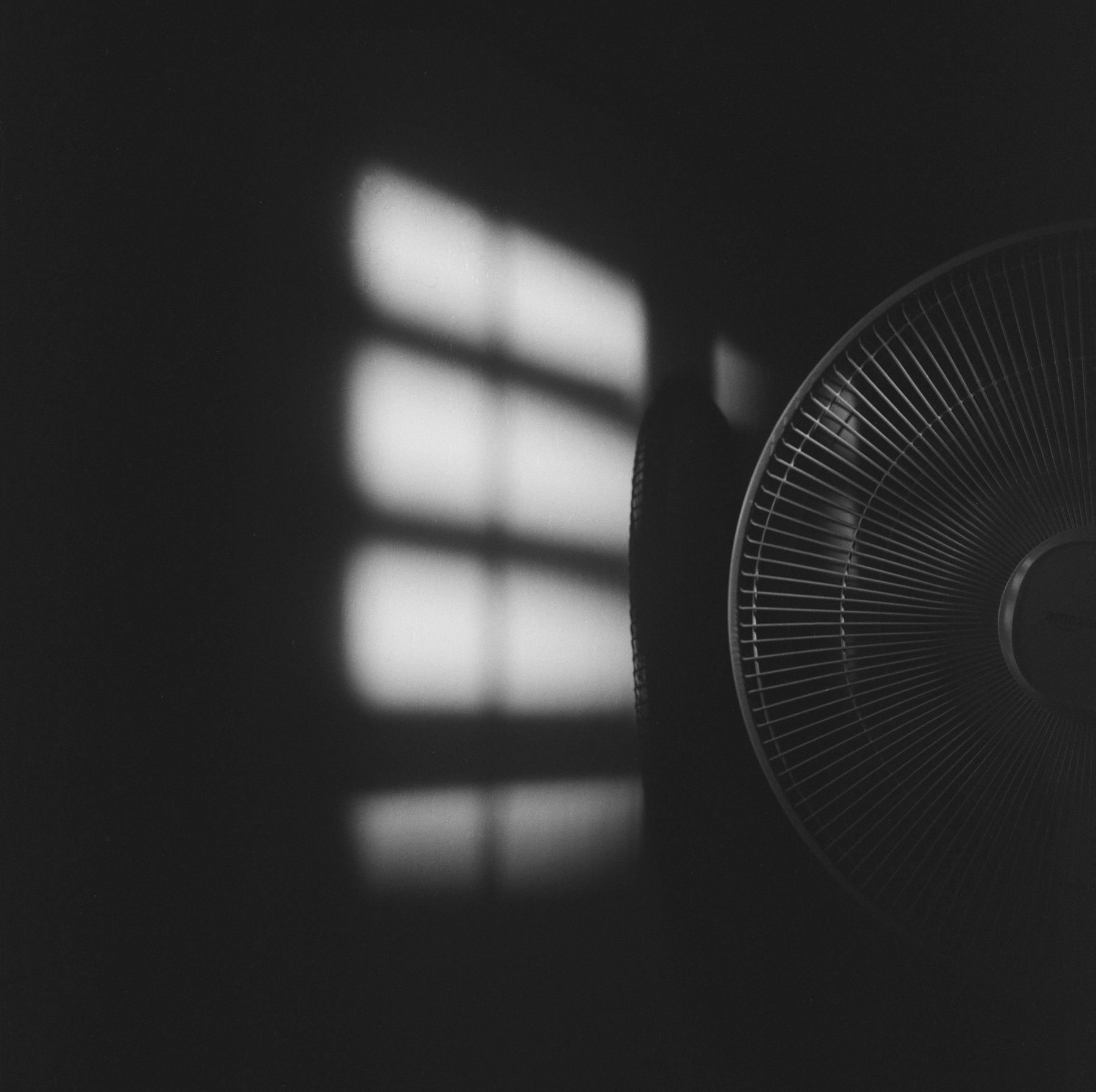 Auto-generated description: A fan is partially visible in the darkness with window shadows cast on the wall nearby.