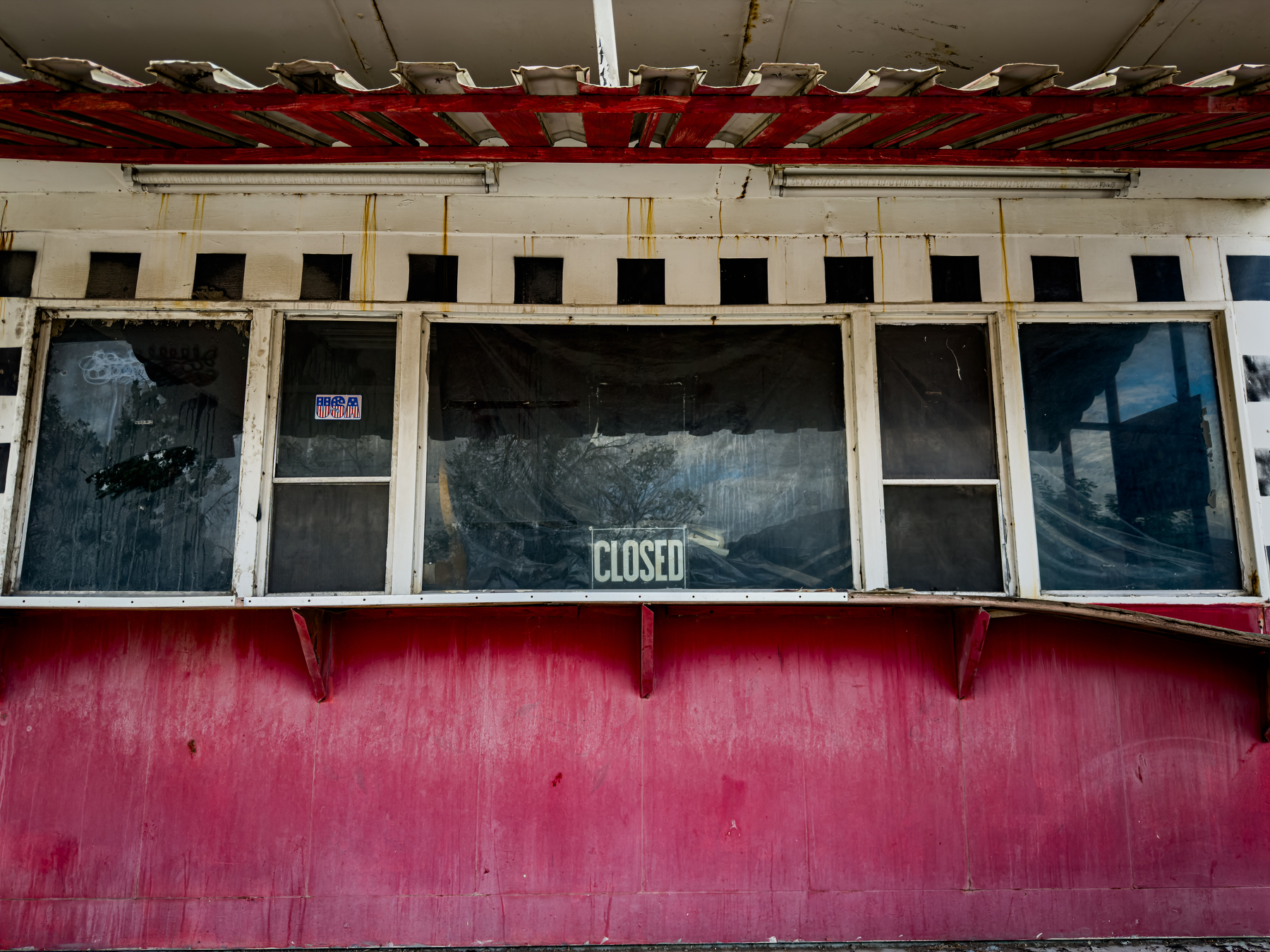 Auto-generated description: An old, weathered concession stand or ticket booth with a CLOSED sign displayed in the center window.