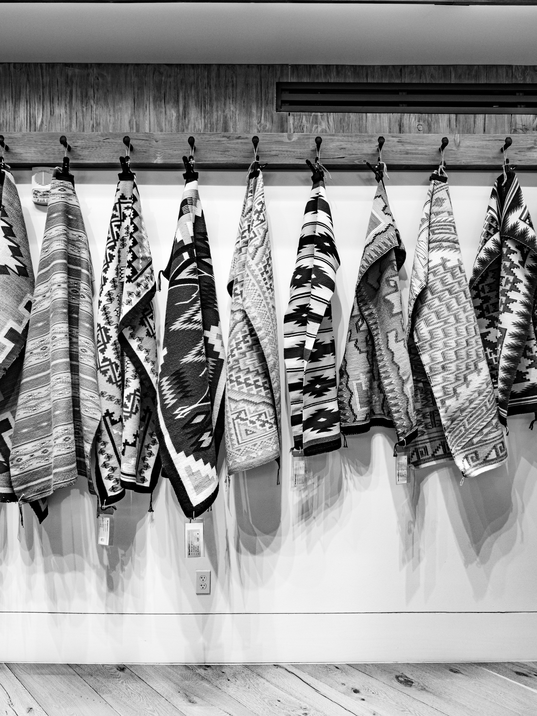 Auto-generated description: Rugs with intricate geometric patterns hang on a wall display in a monochrome setting.