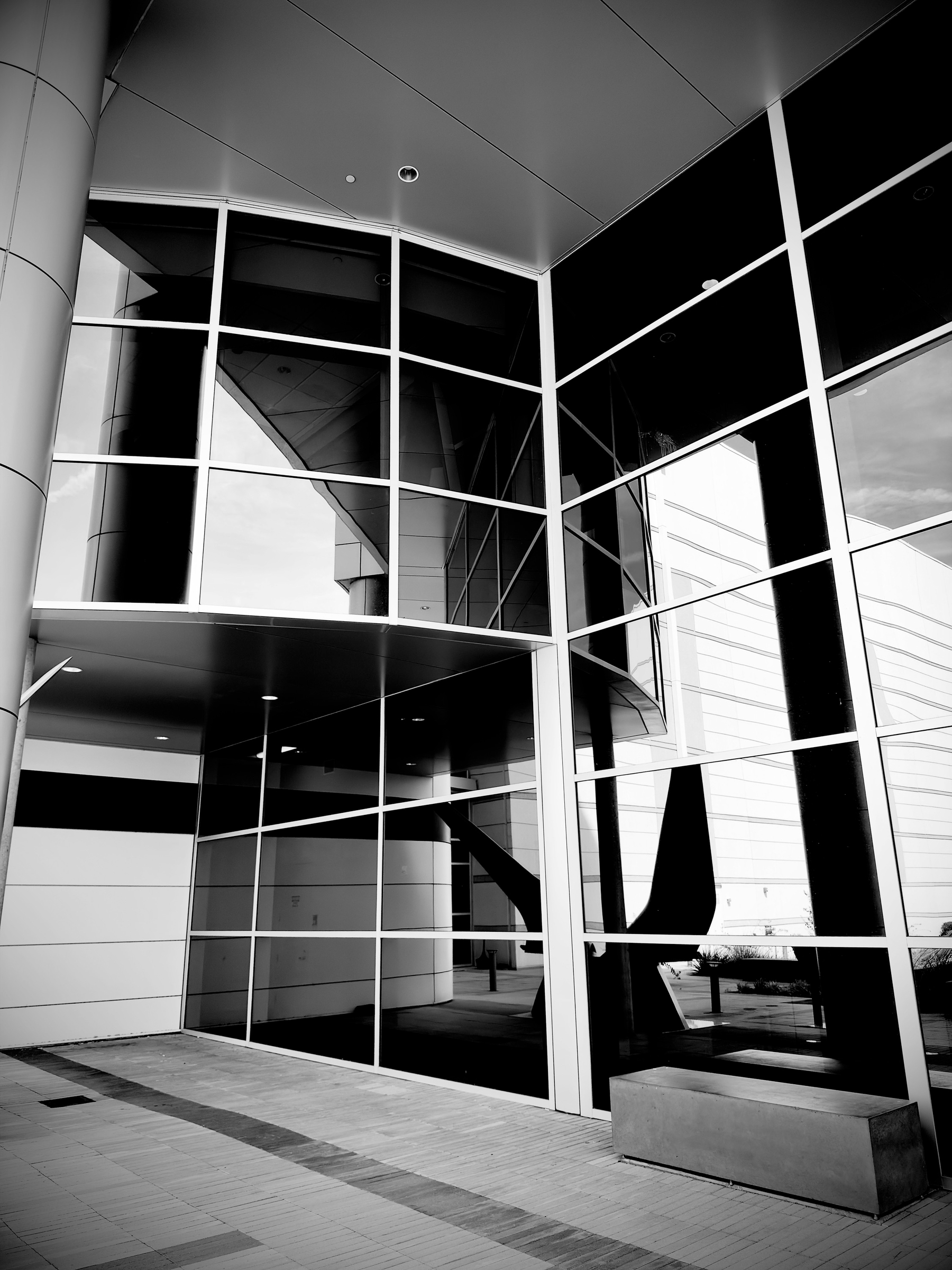 Auto-generated description: A modern building facade featuring large reflective glass windows and sleek architectural lines is shown in black and white.