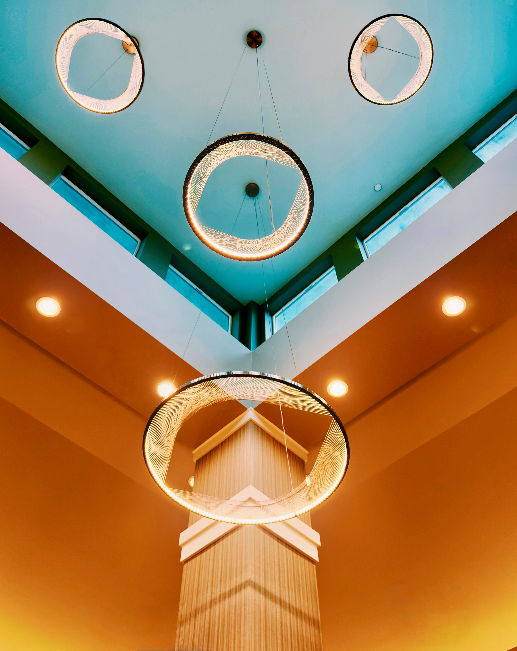 Auto-generated description: A modern ceiling features circular, glowing light fixtures arranged in an artistic pattern, complemented by angular architectural elements and a soft, warm color palette.