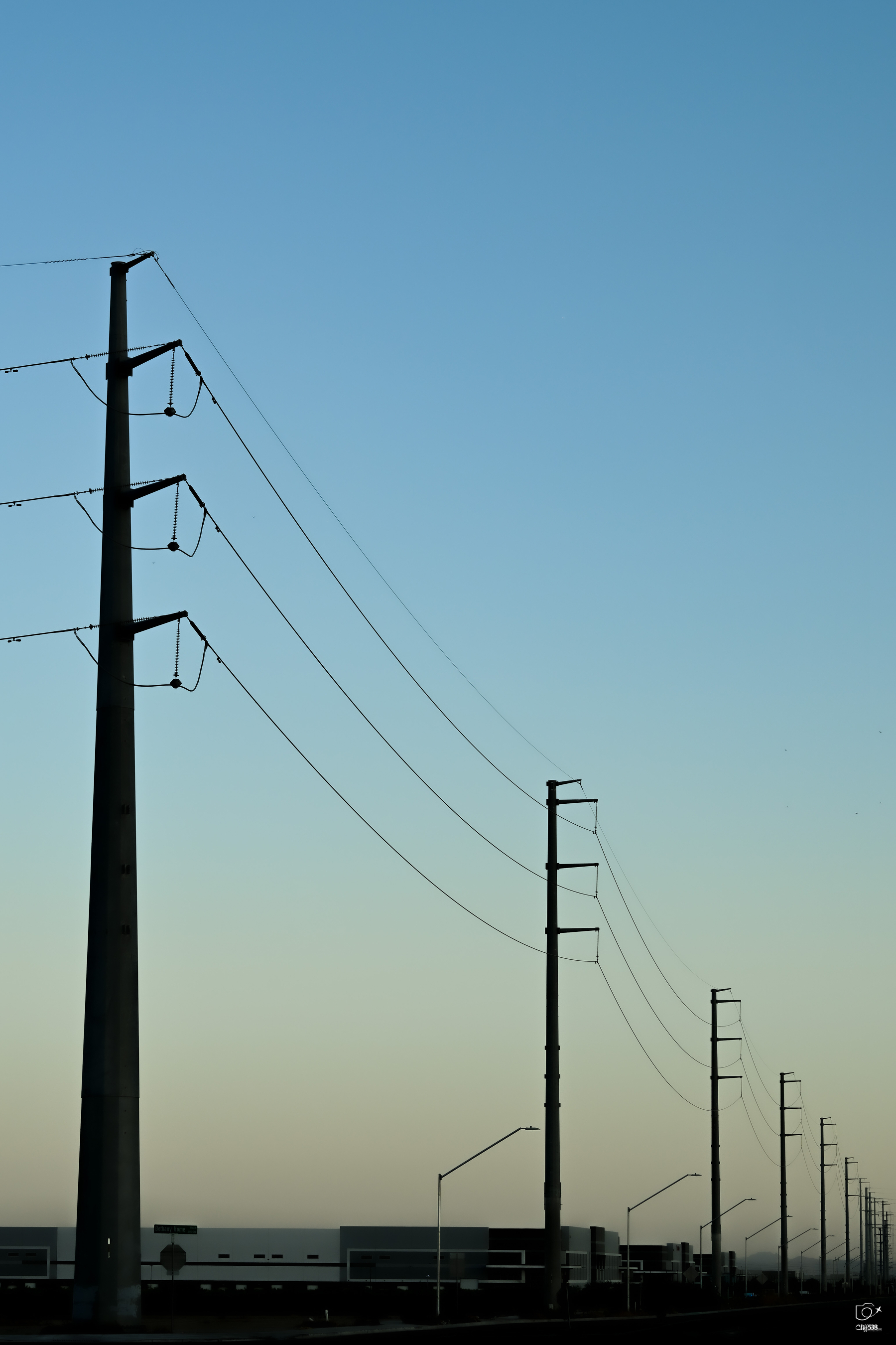 Auto-generated description: Tall power lines stretch across a landscape under a clear sky.