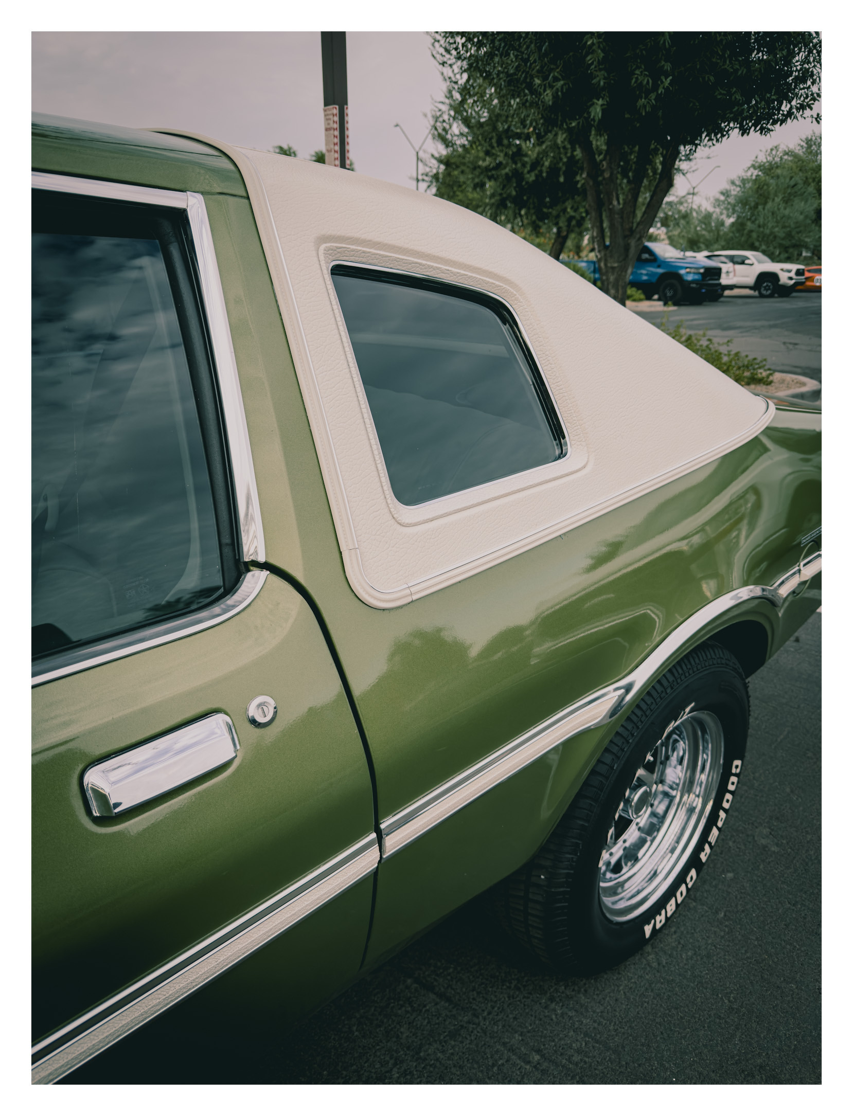 Auto-generated description: A green vintage car with a cream-colored vinyl roof and chrome accents is parked on a paved surface.