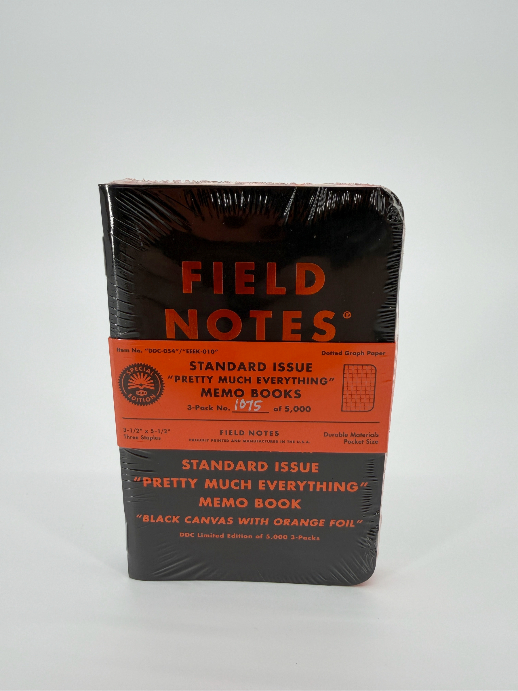 Auto-generated description: A pack of Field Notes memo books with a black cover and orange detailing is sealed in transparent wrap.