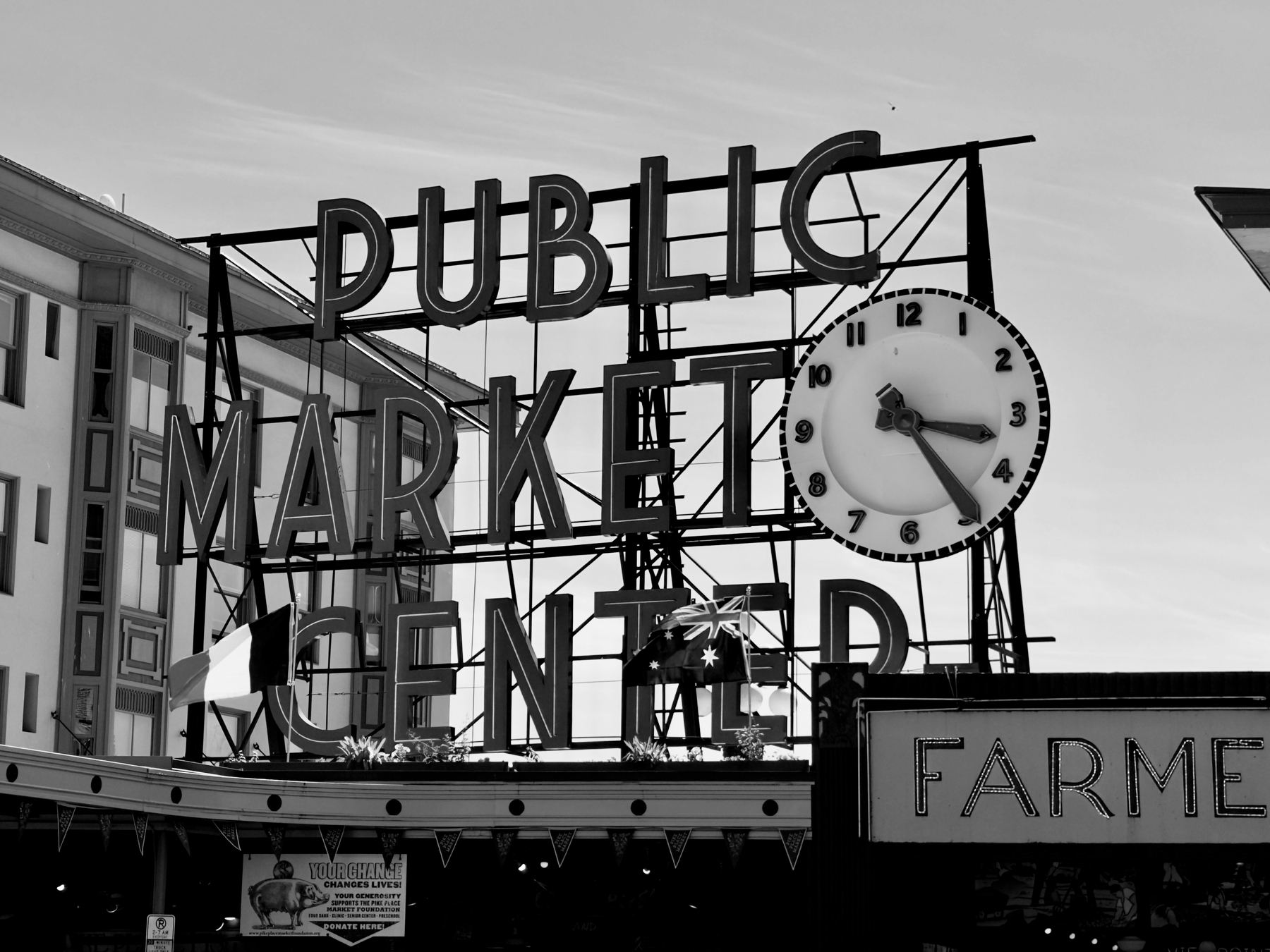 Auto-generated description: A black and white photo of the PUBLIC MARKET CENTER sign with a large clock and a building in the background.