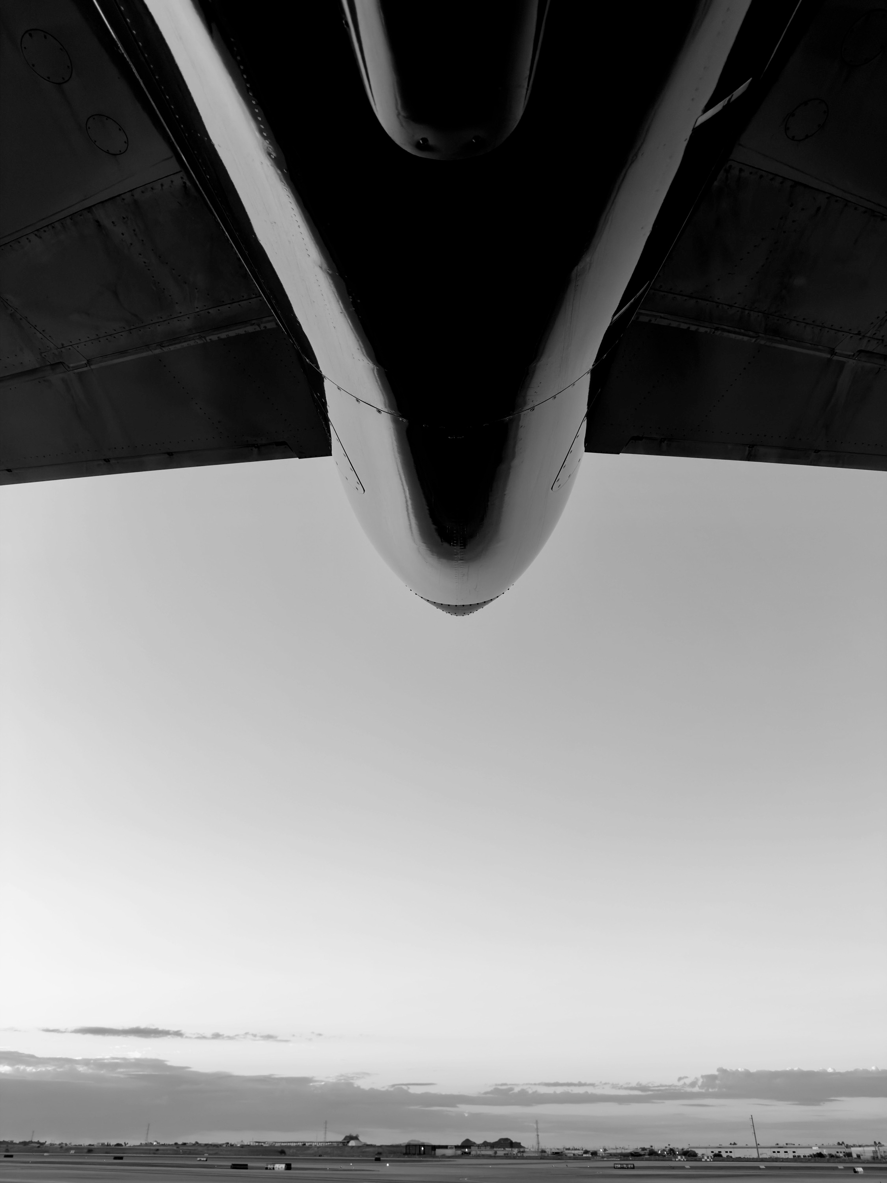 Auto-generated description: The black and white photo captures the underside of an aircraft's wing, with a vast landscape and horizon stretching below.