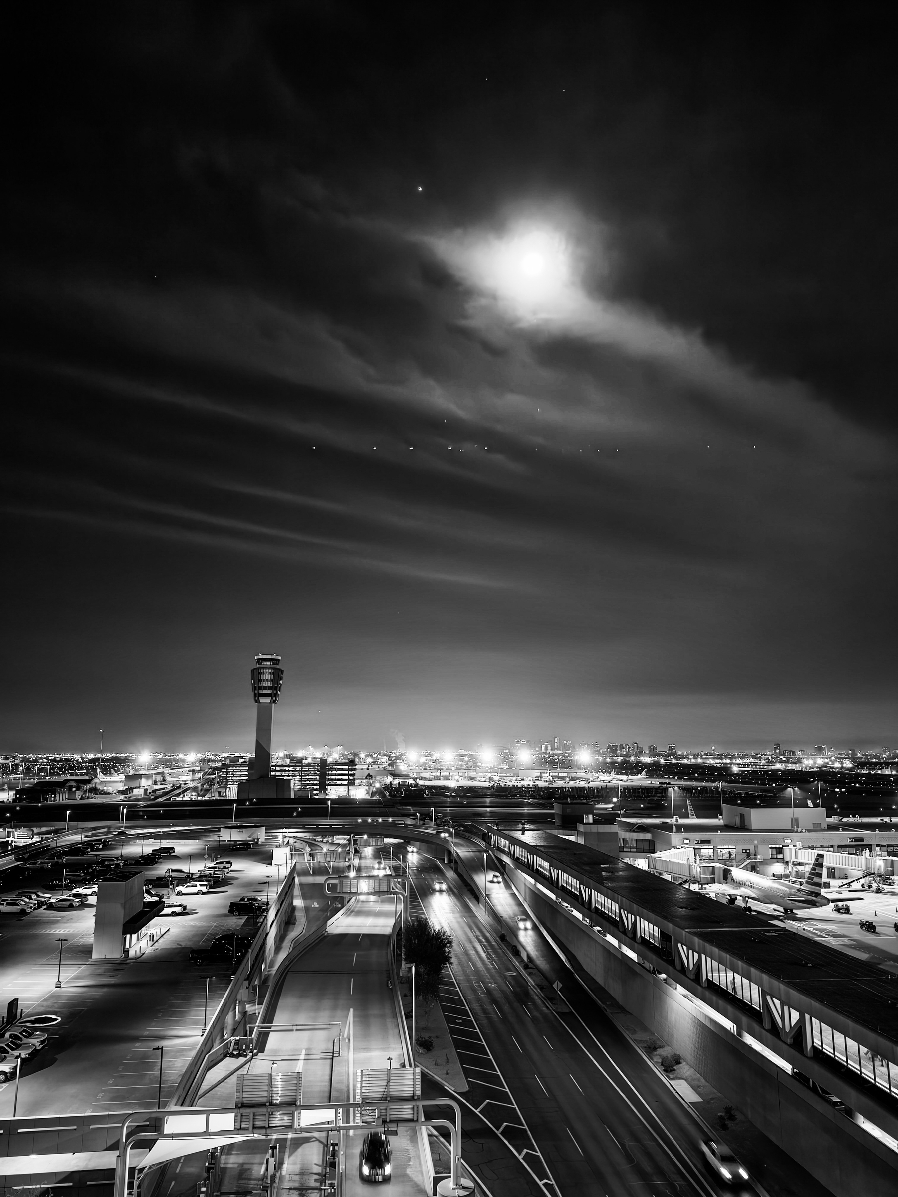 Auto-generated description: A nighttime cityscape features a brightly lit airport with an air traffic control tower and a full moon illuminating the sky.