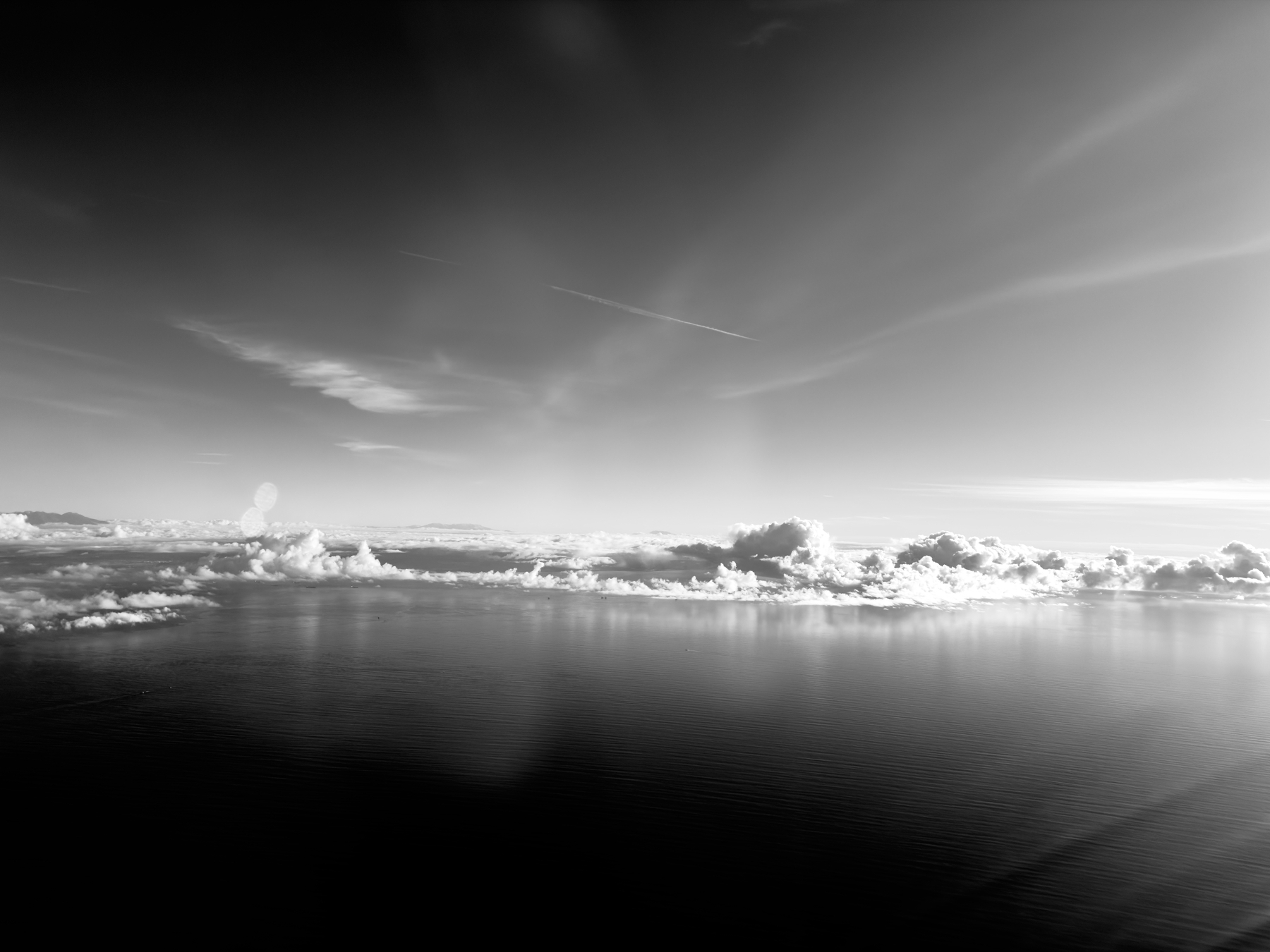 Auto-generated description: A serene, black-and-white scene of fluffy clouds floating over a vast, calm body of water under a partly cloudy sky.