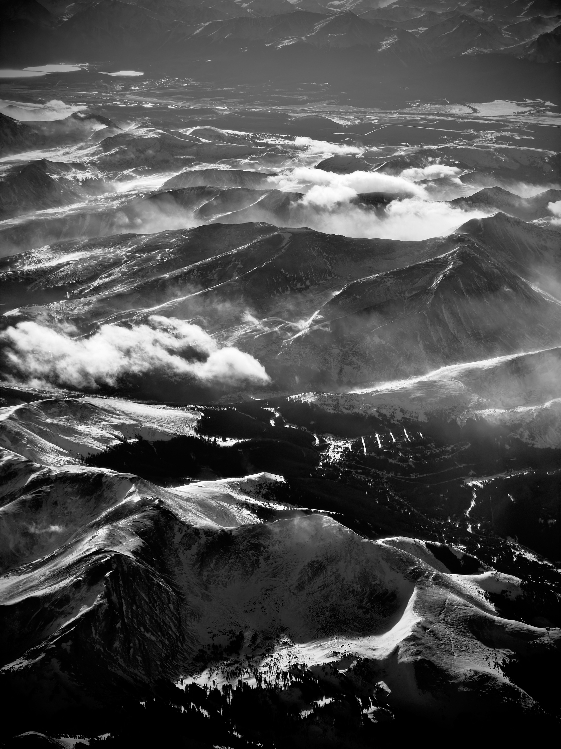 Auto-generated description: A black and white aerial view showcases a vast mountainous landscape with rolling clouds and valleys.
