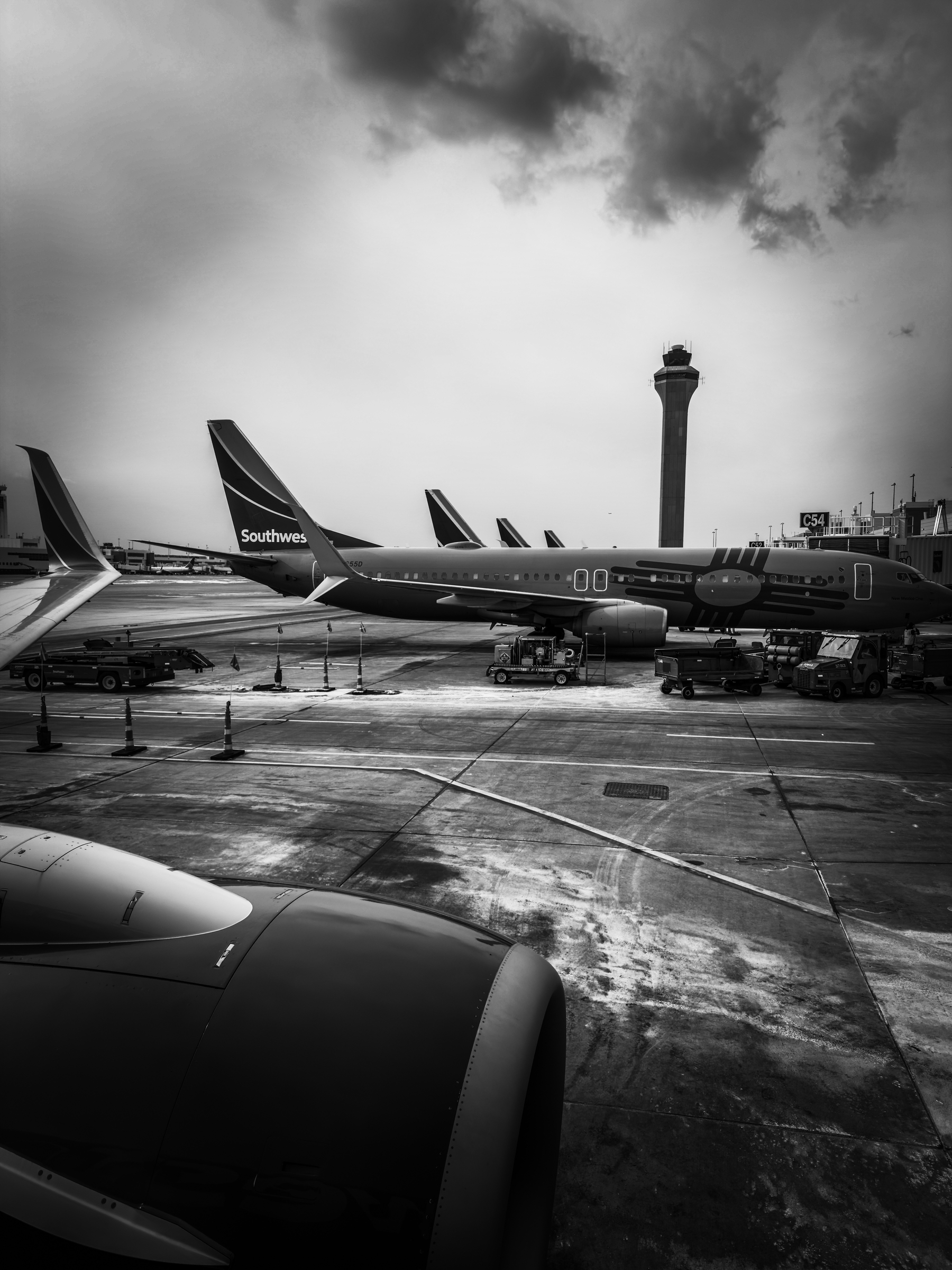 Airplanes are parked at an airport with a control tower in the background under a cloudy sky.