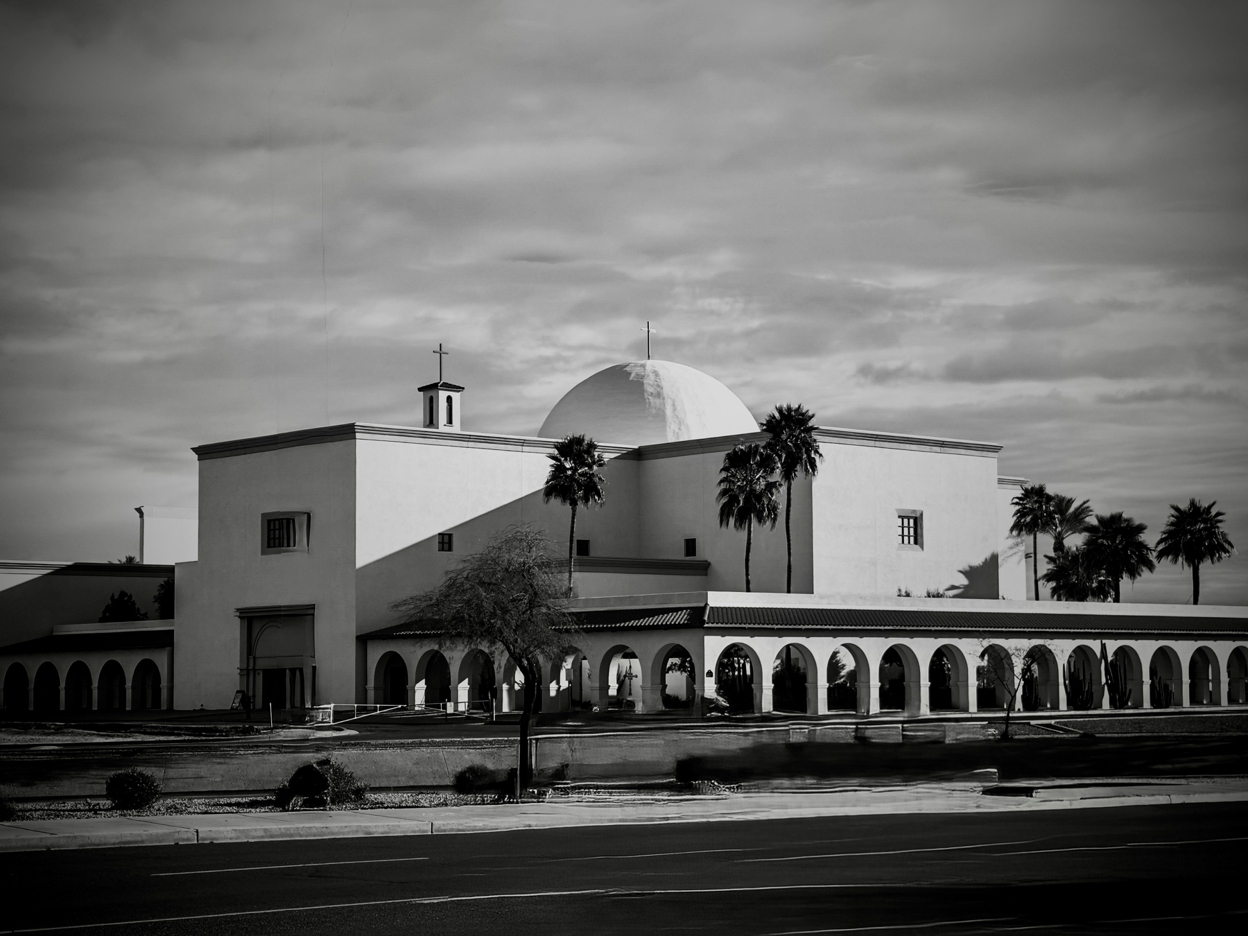 Auto-generated description: A historic mission-style church with a large dome and palm trees is set against a cloudy sky.
