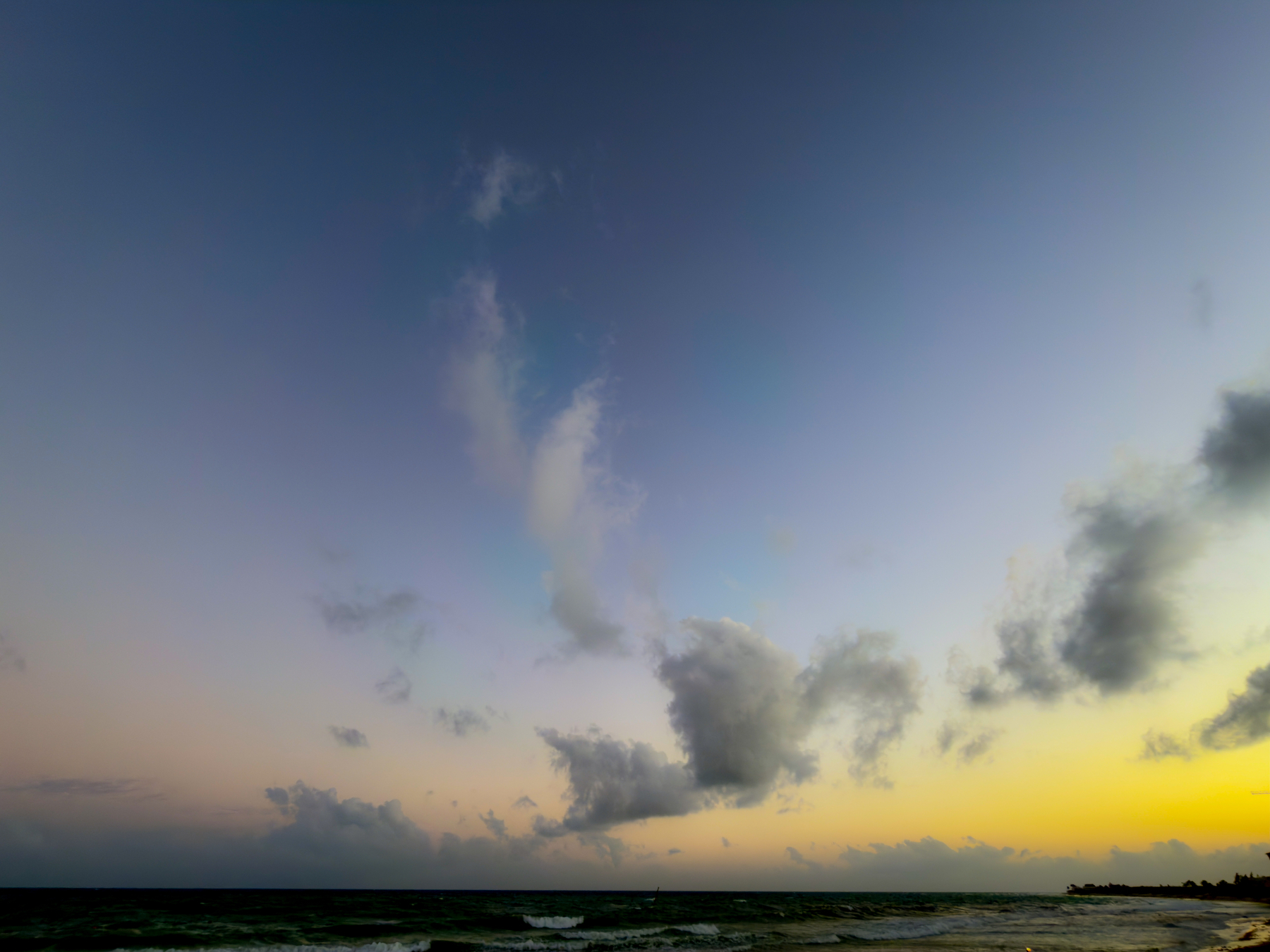 Auto-generated description: A serene ocean view at sunset features a wide sky with scattered clouds and a gently lit horizon.
