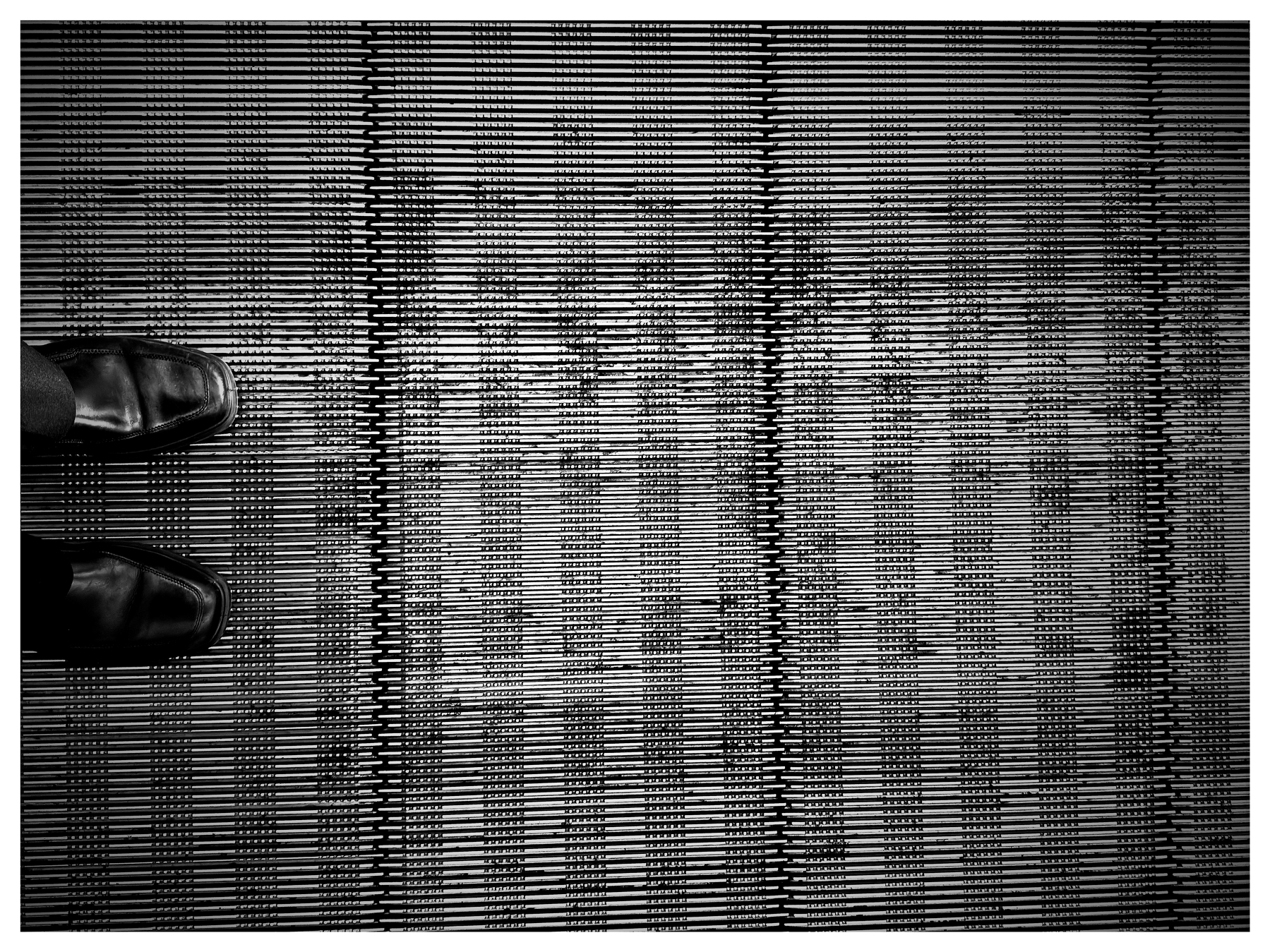 Auto-generated description: A pair of black shoes stands on a metallic moving walkway or escalator step.