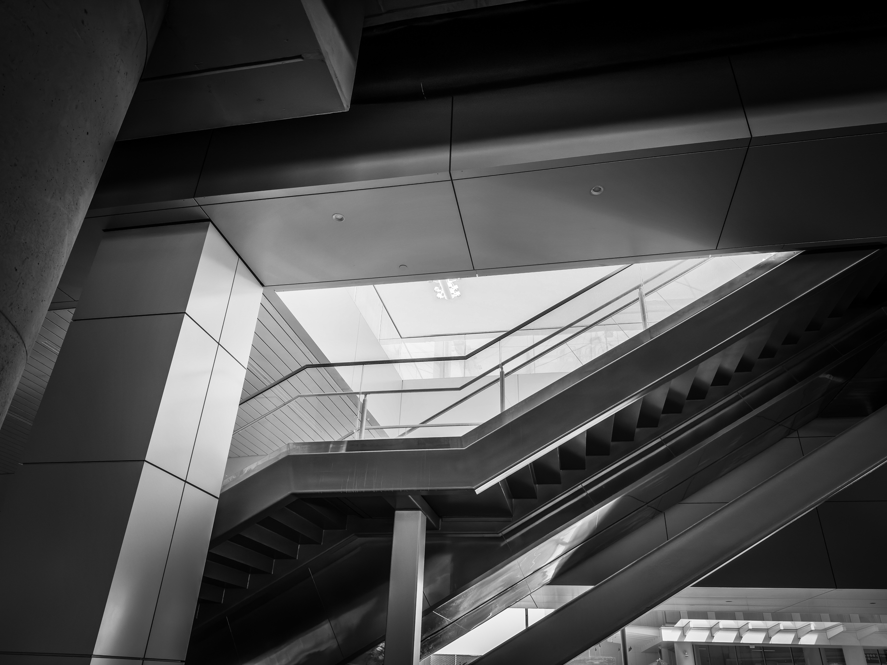 Auto-generated description: A black and white photo of a modern building's interior featuring angular architecture and stairs leading upward.