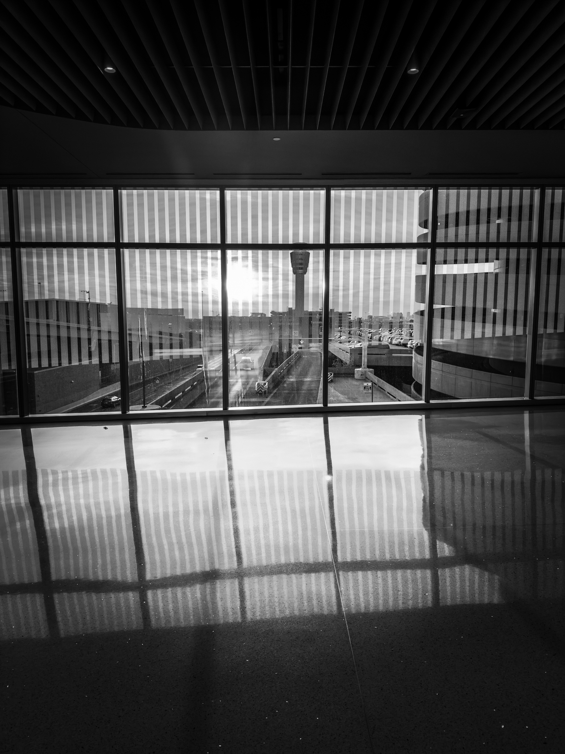 Auto-generated description: A corridor with large windows reflects light, providing a view of an airport control tower in the distance.