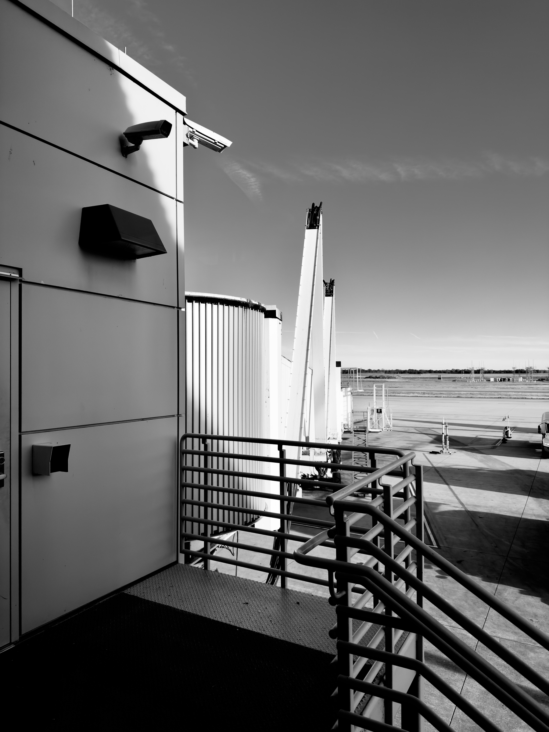 Auto-generated description: A black and white view of an airport jetway leading to a parked airplane on the tarmac.