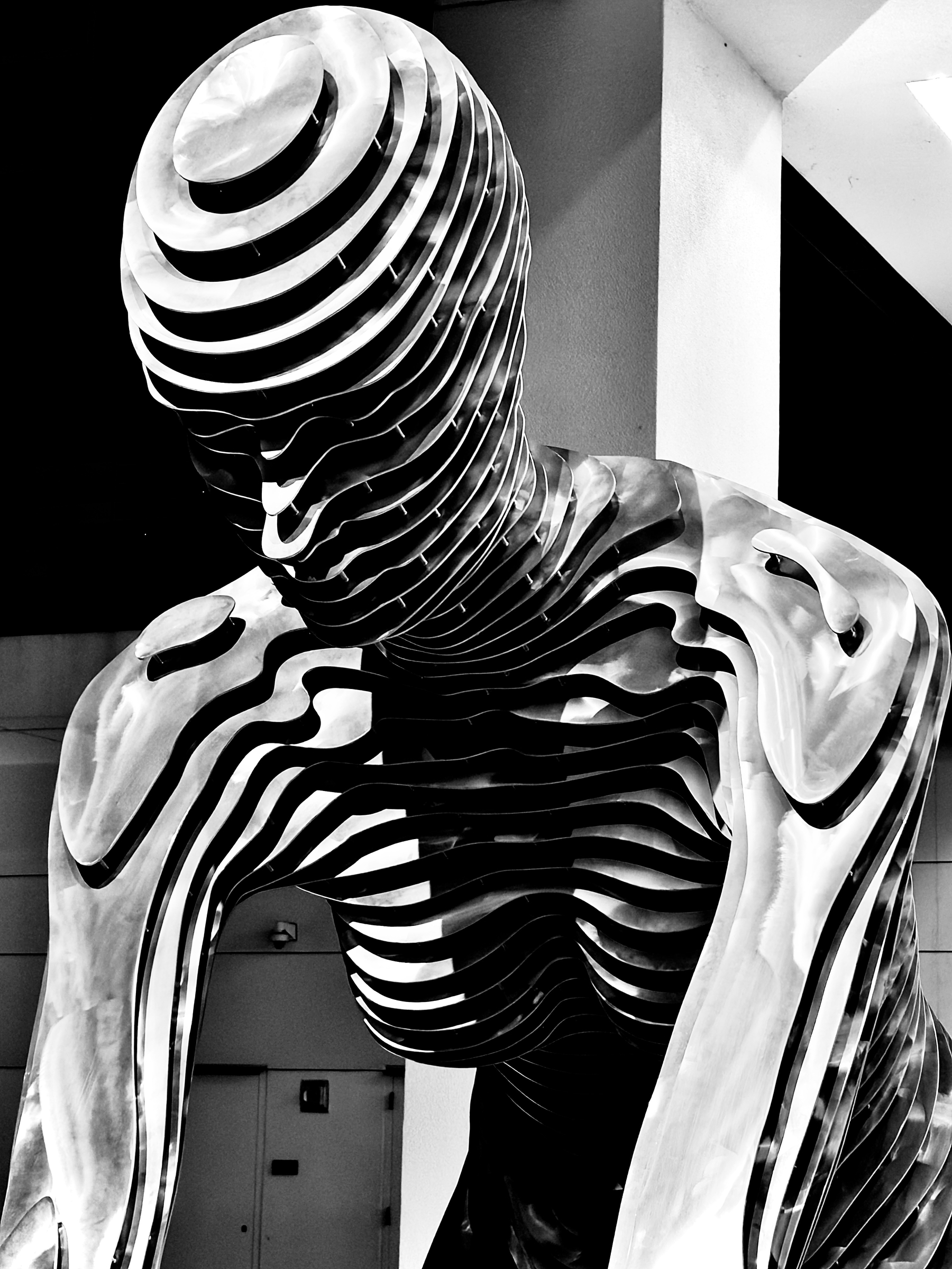 Auto-generated description: A modern, abstract sculpture made of layered metal pieces is depicted in a monochrome setting.