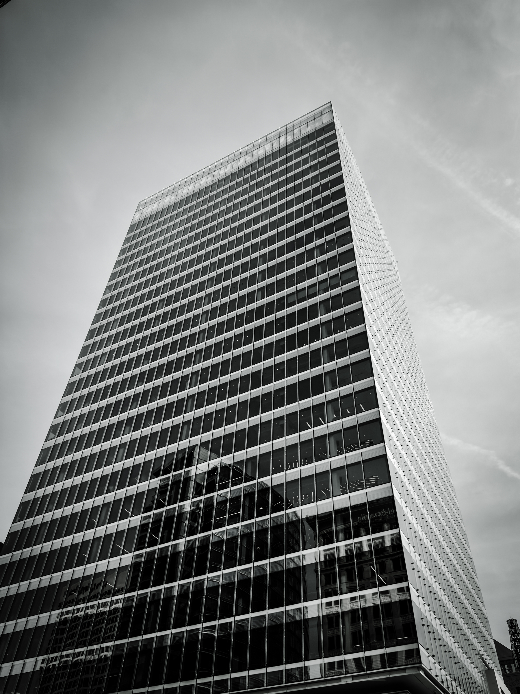 Auto-generated description: A tall, modern skyscraper with a glass facade rises against a cloudy sky.