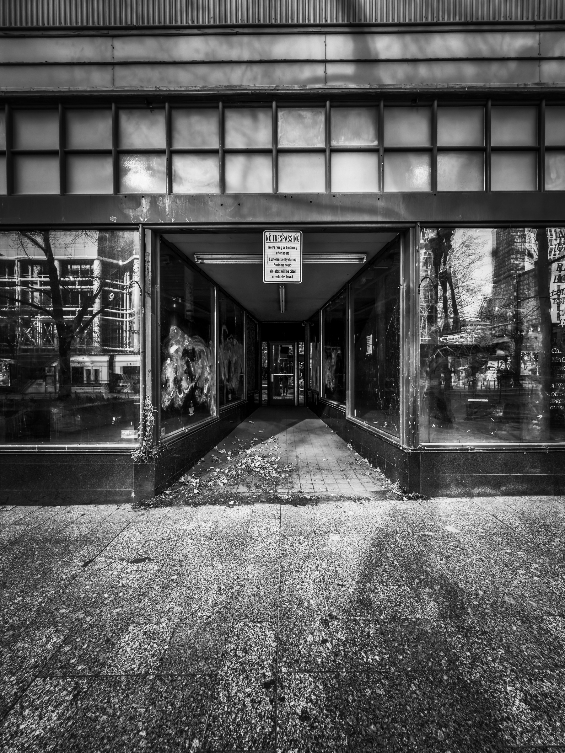 Auto-generated description: A black and white photo shows the entrance to an abandoned building with boarded windows and a No Trespassing sign.