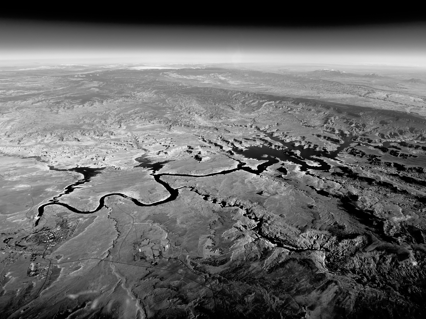 Auto-generated description: A vast, aerial view of a rugged landscape features a winding river or canyon, surrounded by arid terrain extending to the horizon.