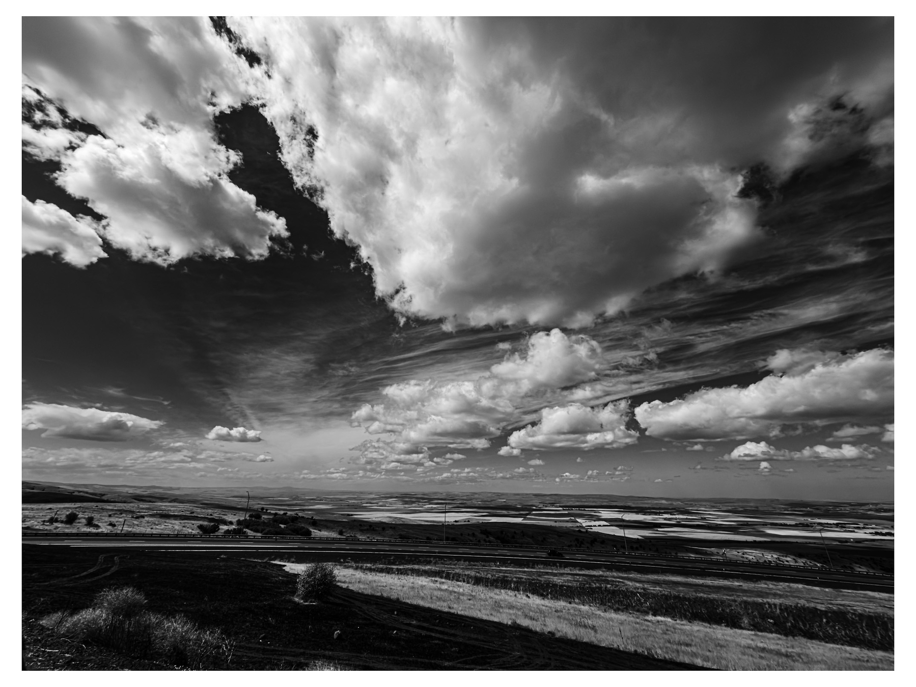 Auto-generated description: A vast landscape under a dramatic sky filled with large, textured clouds stretches out to the horizon.